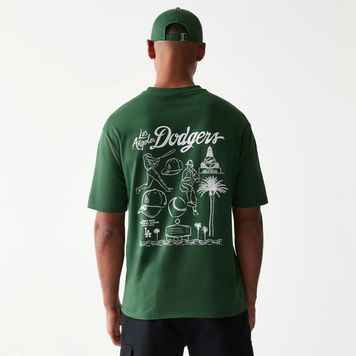 New Era LA Dodgers MLB Baseball Graphic Dark Green Oversized T-Shirt, back view on a model showing a white graphic with baseball figures, the Dodgers logo across the shoulders and various Los Angeles landmarks beneath.