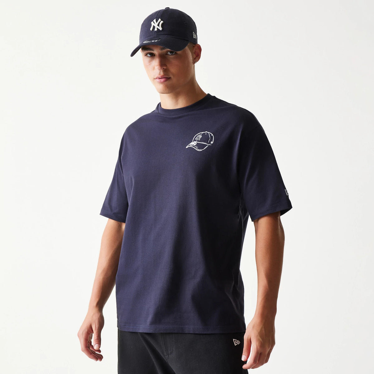New Era New York Yankees MLB Baseball Graphic Navy Oversized T-Shirt, front view on-model showing a white embroidered cap graphic on the left chest and a New Era logo on the left sleeve, paired with a matching New York Yankees cap.