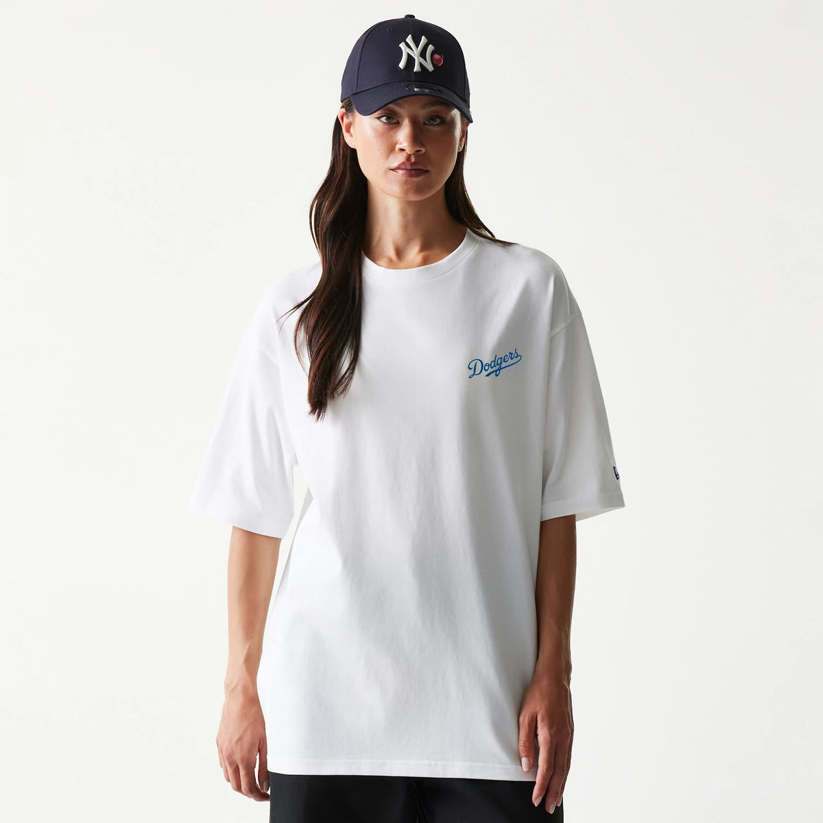 New Era LA Dodgers MLB World Series White T-Shirt, front view on-model featuring the embroidered Dodgers logo in blue on the left chest, short sleeves, and a relaxed fit, styled with a dark cap and black trousers.