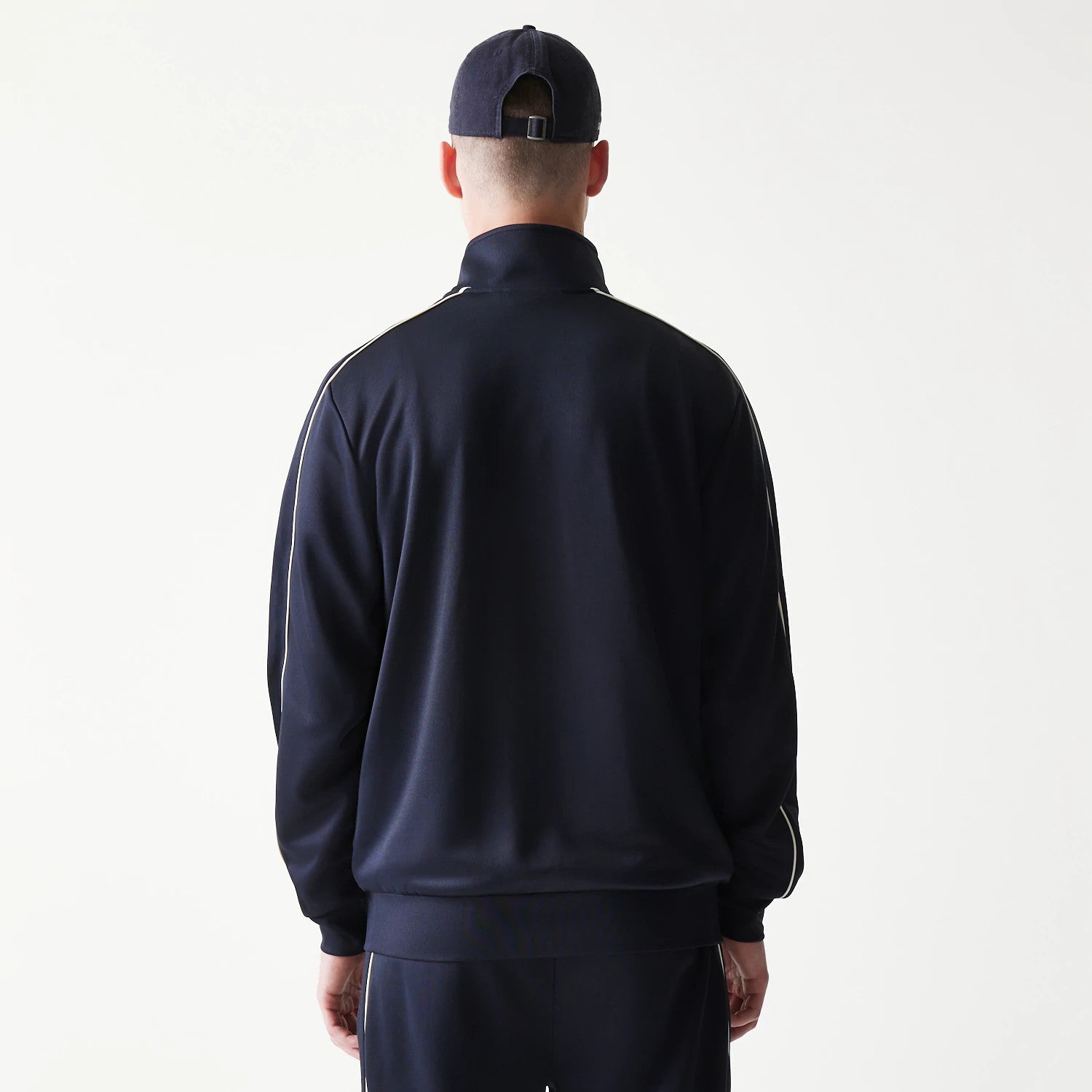 New Era New York Yankees MLB Piping Navy Track Jacket, back view showing the plain navy back with white piping along the shoulders and sleeves on a model wearing a matching navy cap.