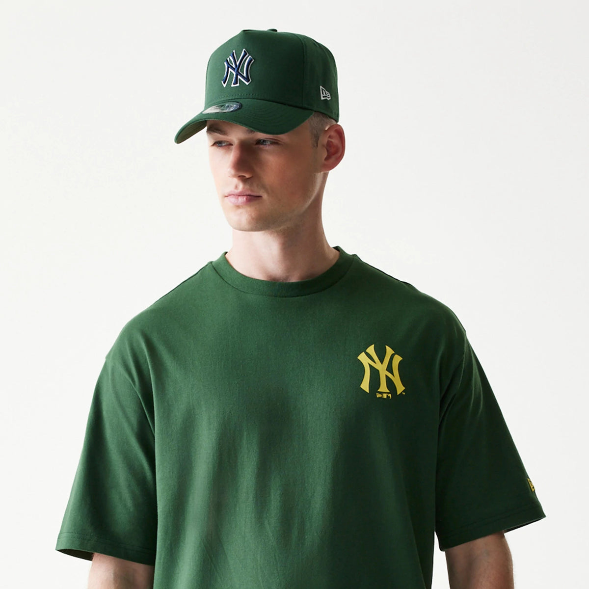 New Era New York Yankees MLB World Series Dark Green T-Shirt, front view on a model with a matching cap, showcasing a yellow embroidered Yankees logo on the left chest and a dark green colour throughout the shirt.