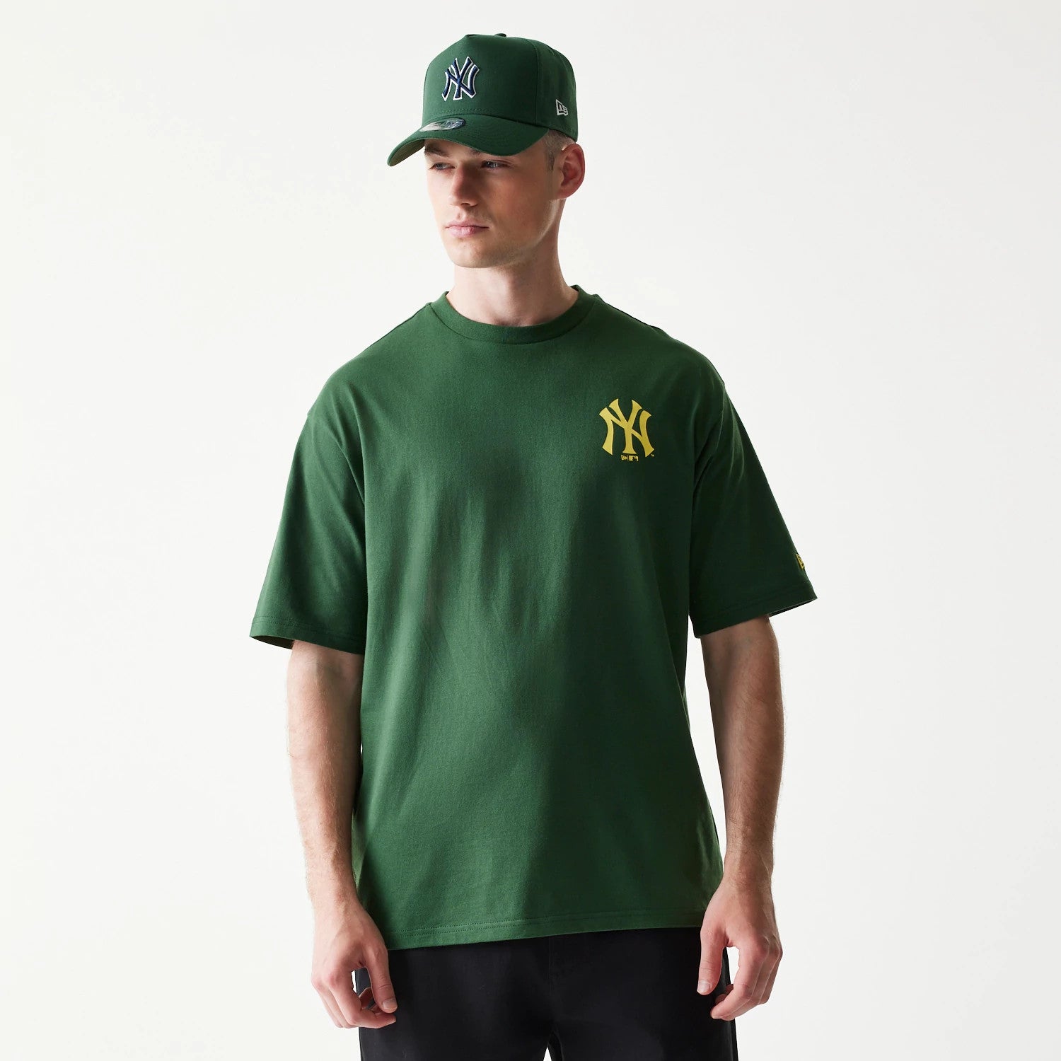 New Era New York Yankees MLB World Series Dark Green T-Shirt, front view on-model showing a yellow embroidered Yankees logo on the left chest, styled with a matching dark green cap featuring the New Era logo on the side.