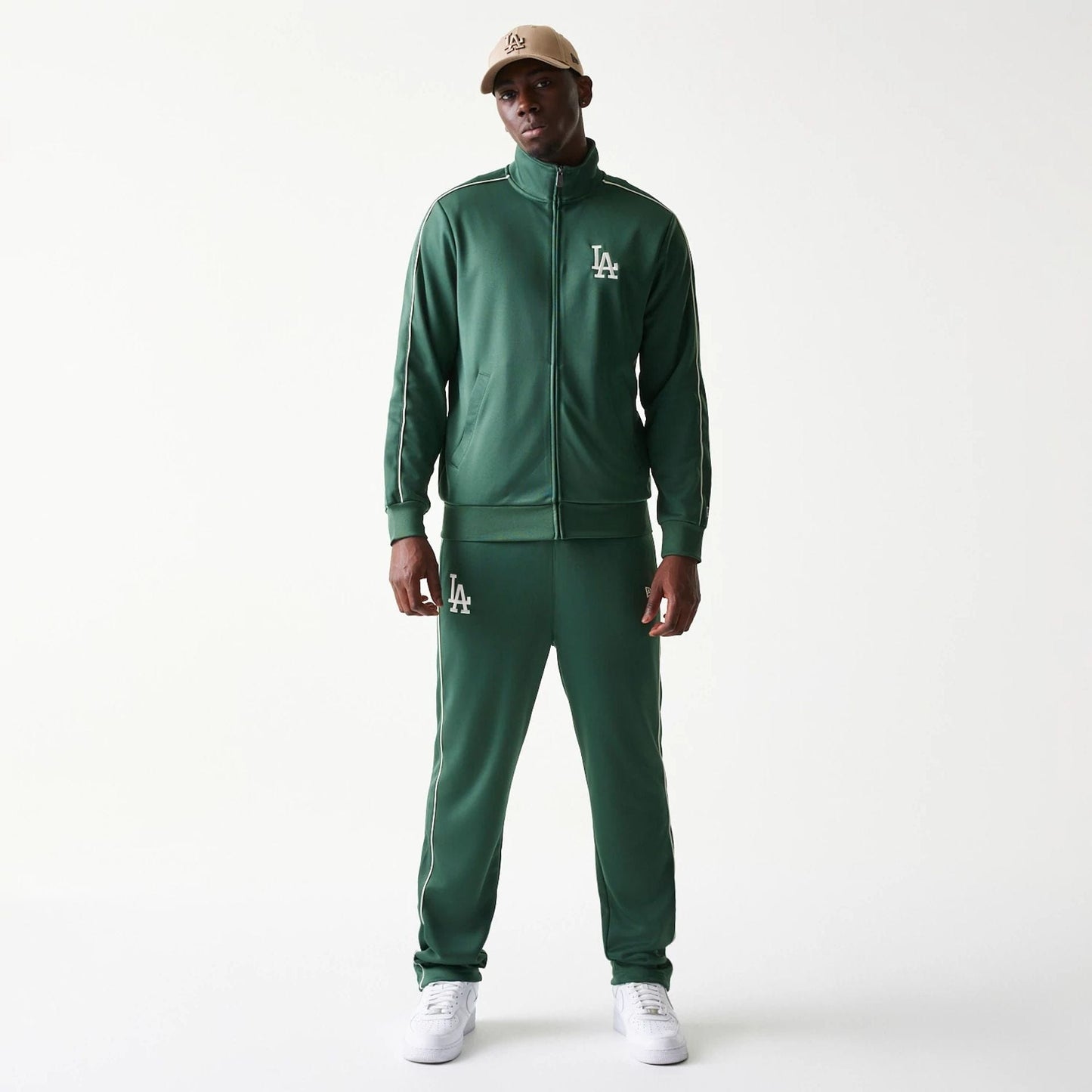 New Era LA Dodgers MLB Piping Dark Green Track Jacket, front view on-model wearing a matching cap, featuring a white embroidered LA logo on the left chest and piping along the shoulders and sleeves, creating a athletic look.