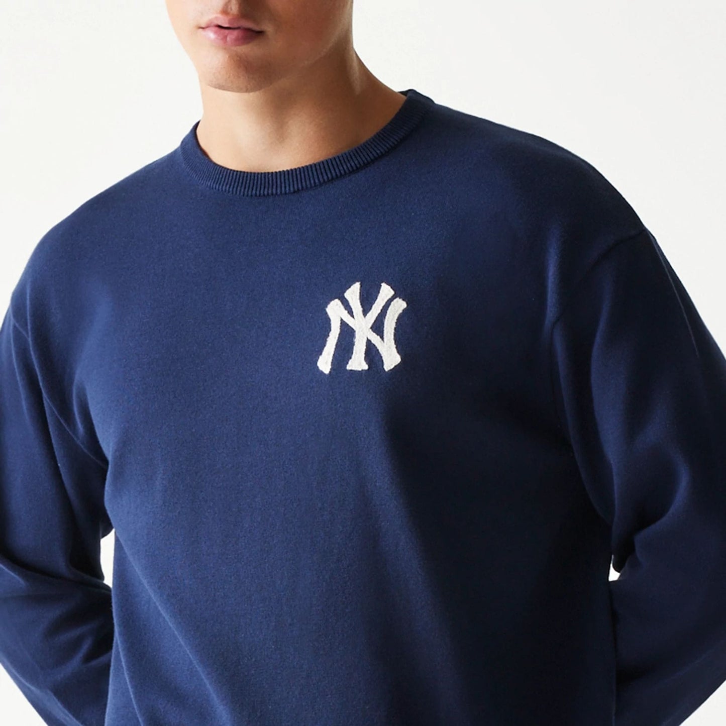 New Era New York Yankees MLB Essential Navy Knitted Sweater, front view on a model showing the white embroidered NY logo on the left chest against the rich navy fabric, with a ribbed crew neck design.