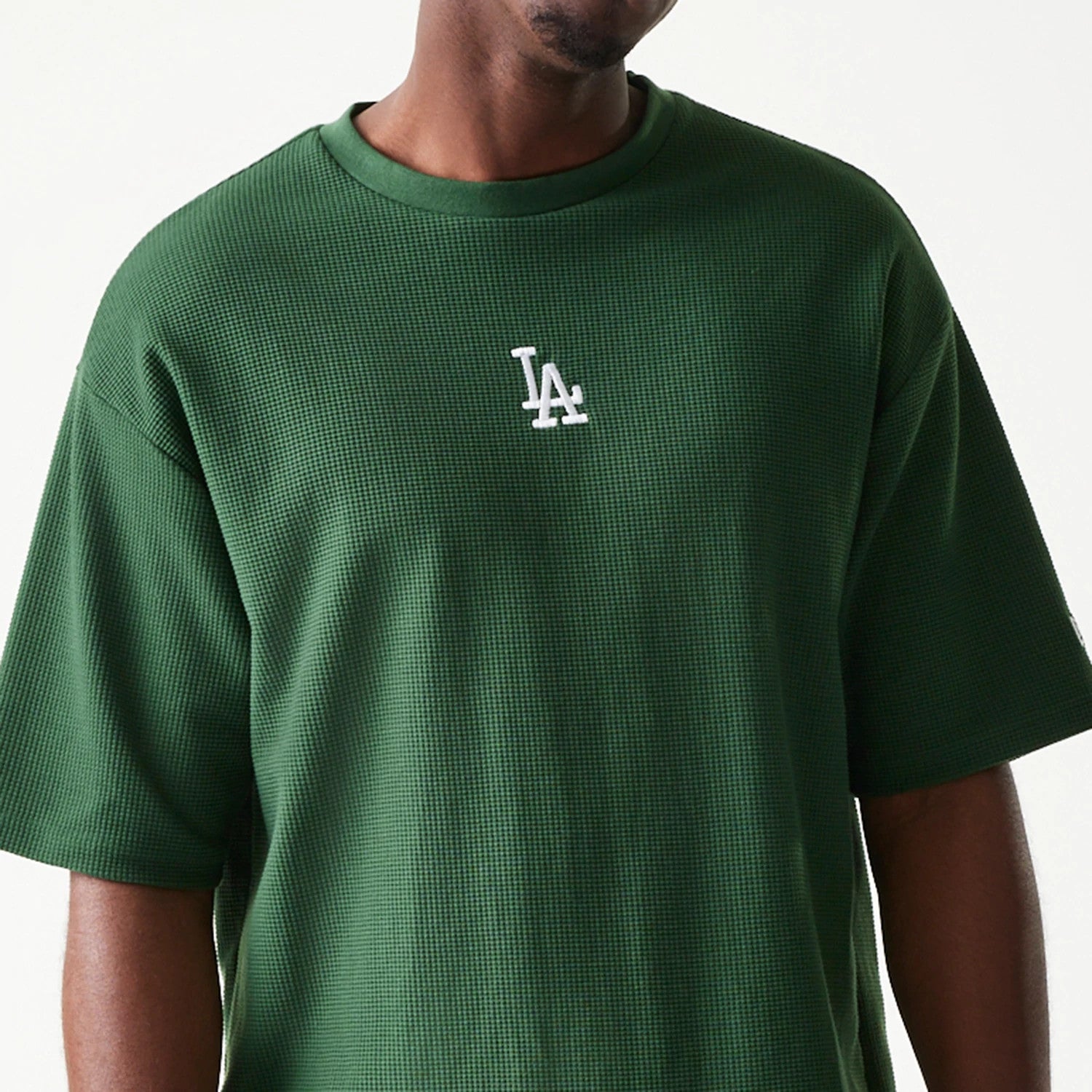 New Era LA Dodgers MLB Waffle Dark Green Oversized T-Shirt, front view showing the white embroidered LA logo centred on the chest of the textured green fabric, worn by a model with casual styling from the waist up.