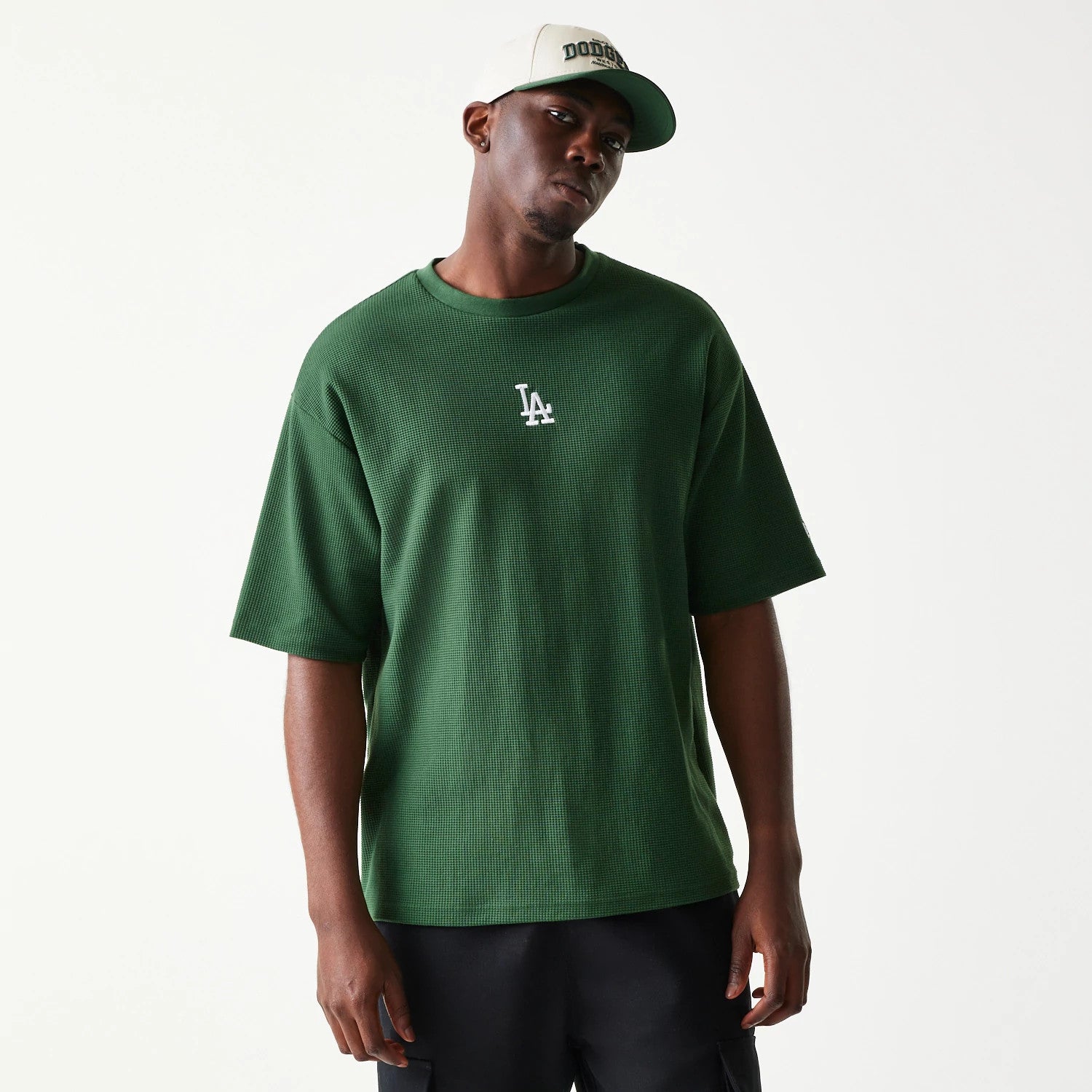 New Era LA Dodgers MLB Waffle Dark Green Oversized T-Shirt, front view on-model showing a large white embroidered LA logo at the centre of the chest and a waffle texture, paired with a white cap featuring Dodgers lettering.