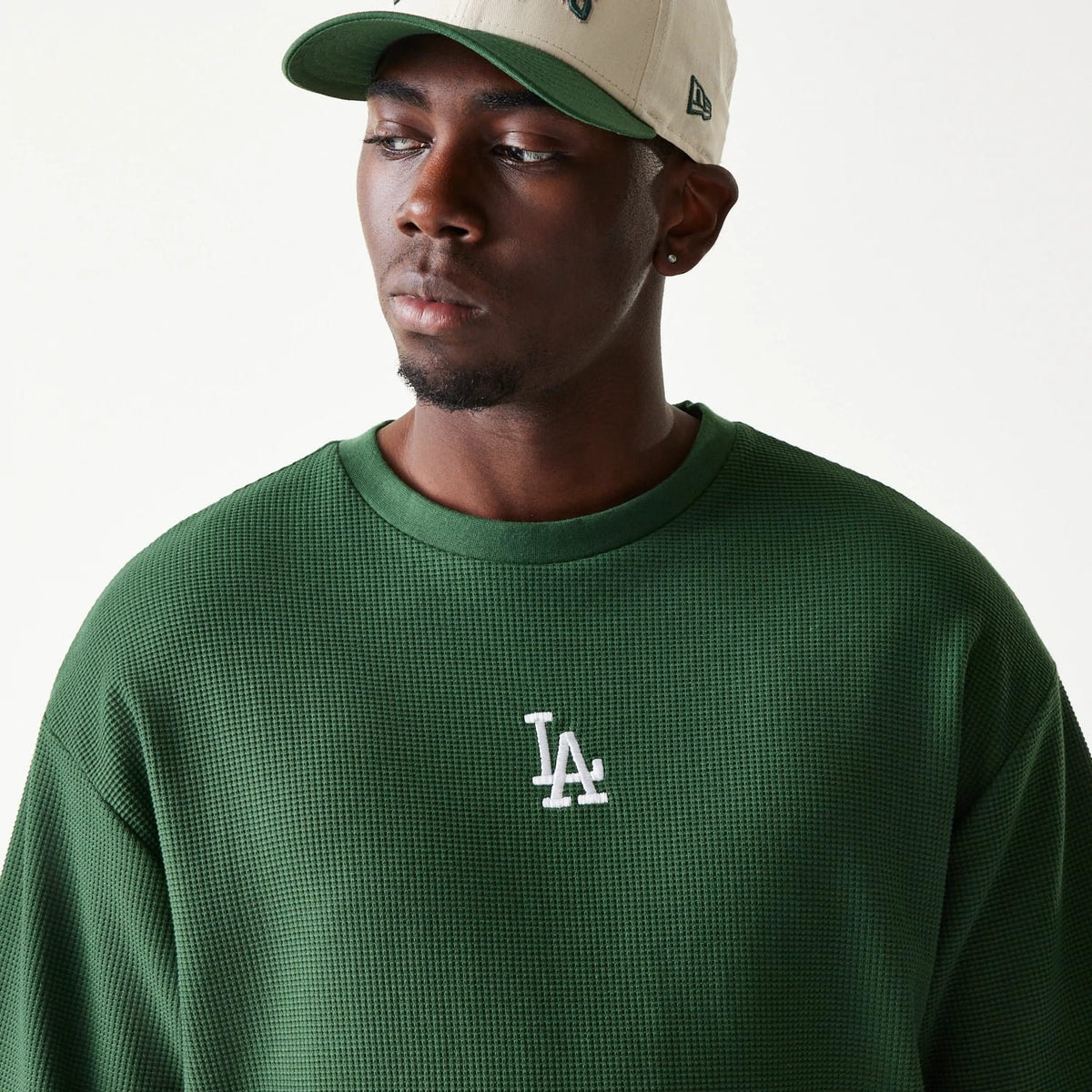 New Era LA Dodgers MLB Waffle Dark Green Oversized T-Shirt, front view on-model showing the textured dark green fabric, with a white embroidered LA logo centred on the chest, styled with a beige cap.