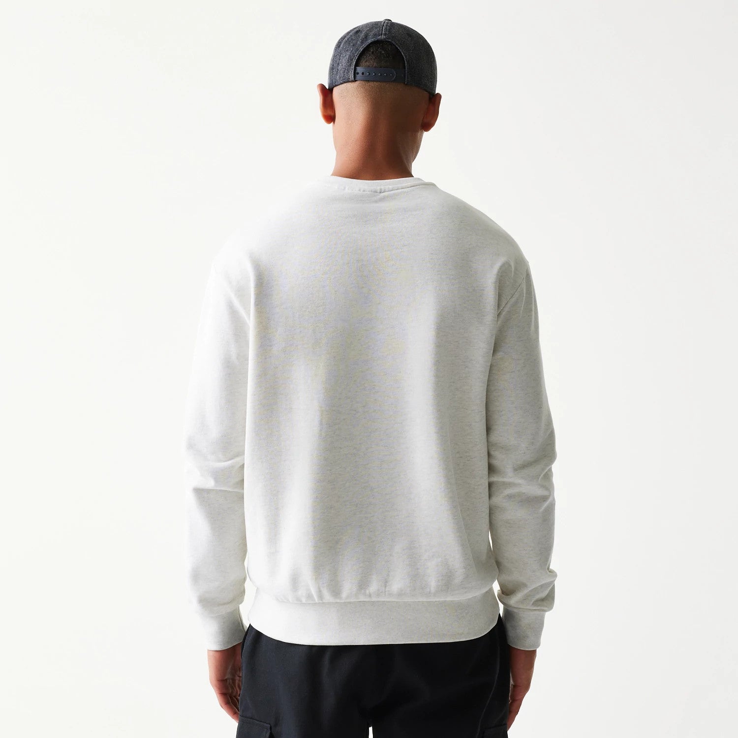 New Era New York Yankees MLB Graphic Pastel Grey Oversized Crew Neck Sweater, back view on a model wearing a dark cap and black trousers, showing a simple grey design with ribbed cuffs and hem.