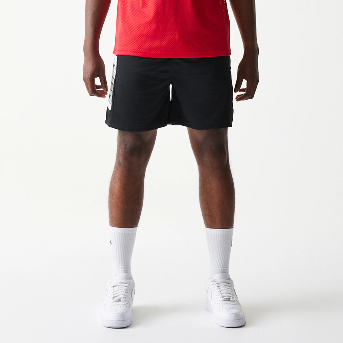 New Era Chicago Bulls NBA Mesh Black Shorts, front view on-model showing the relaxed fit with white vertical BLOCK lettering on the right leg and a plain black design paired with white socks and trainers.