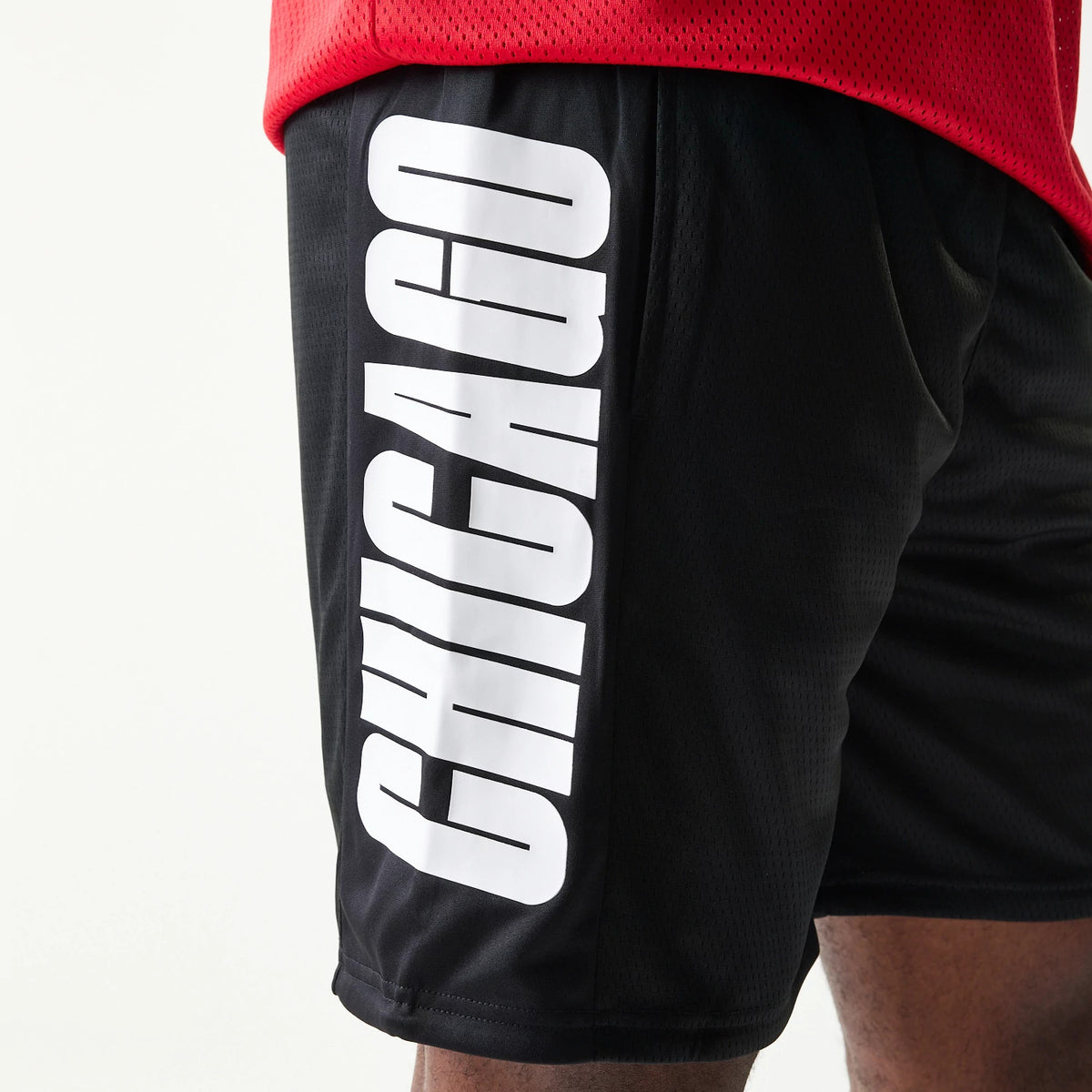 New Era Chicago Bulls NBA Mesh Black Shorts, side view showing white CHICAGO lettering running vertically down the side of the black fabric, with a close fit seen on the model's leg.