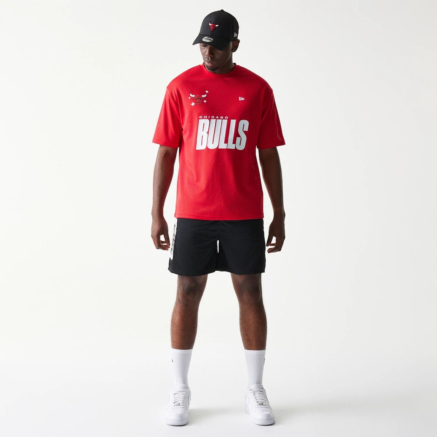 New Era Chicago Bulls NBA Mesh Black Shorts, front view on-model showing the plain black mesh design reaching above the knee, paired with a red Bulls T-shirt and a black cap, enhancing the sports look.