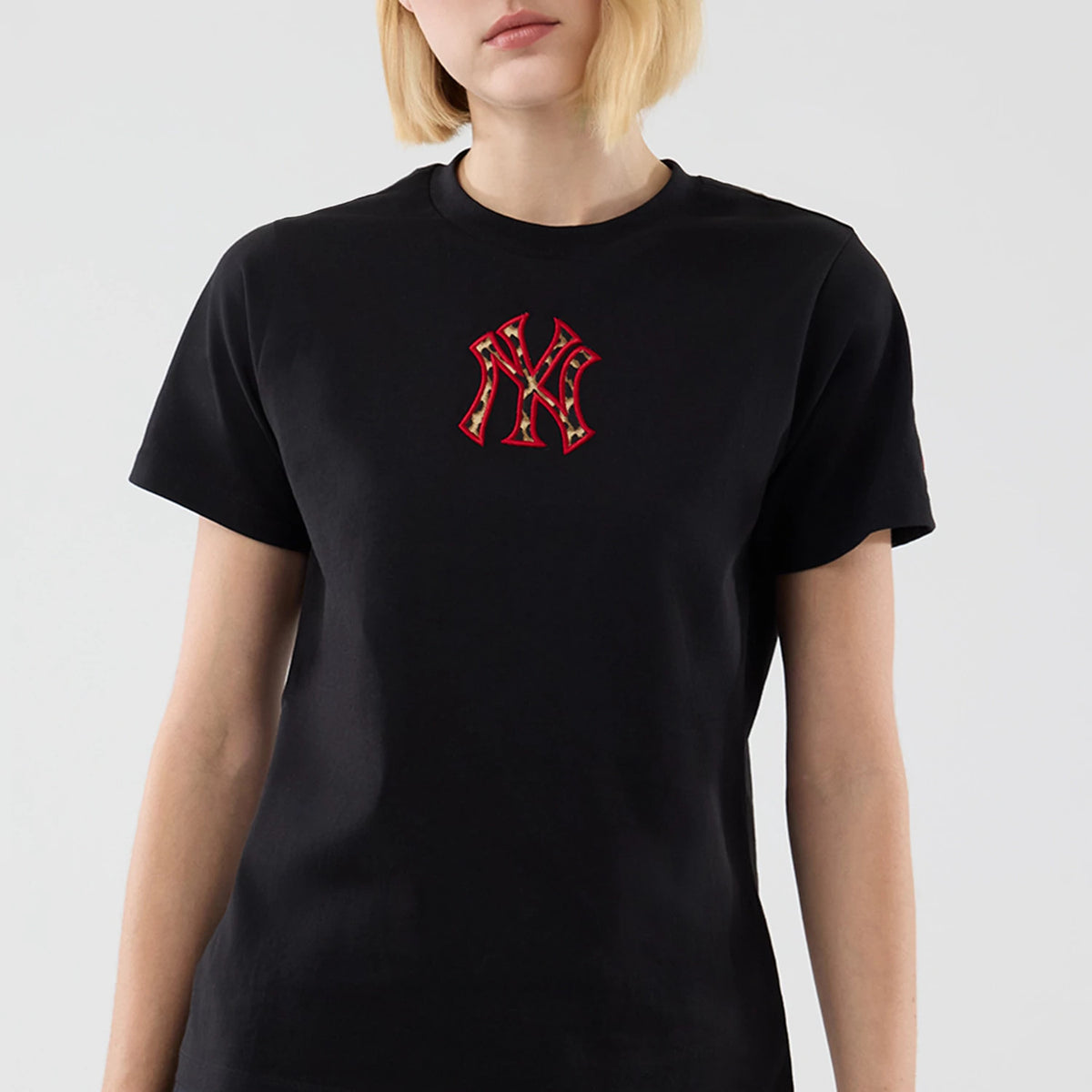 New Era New York Yankees Womens MLB Infill Black T-shirt, front view on-model showing a red and gold embroidered NY logo centred on the chest against the plain black fabric with short sleeves.