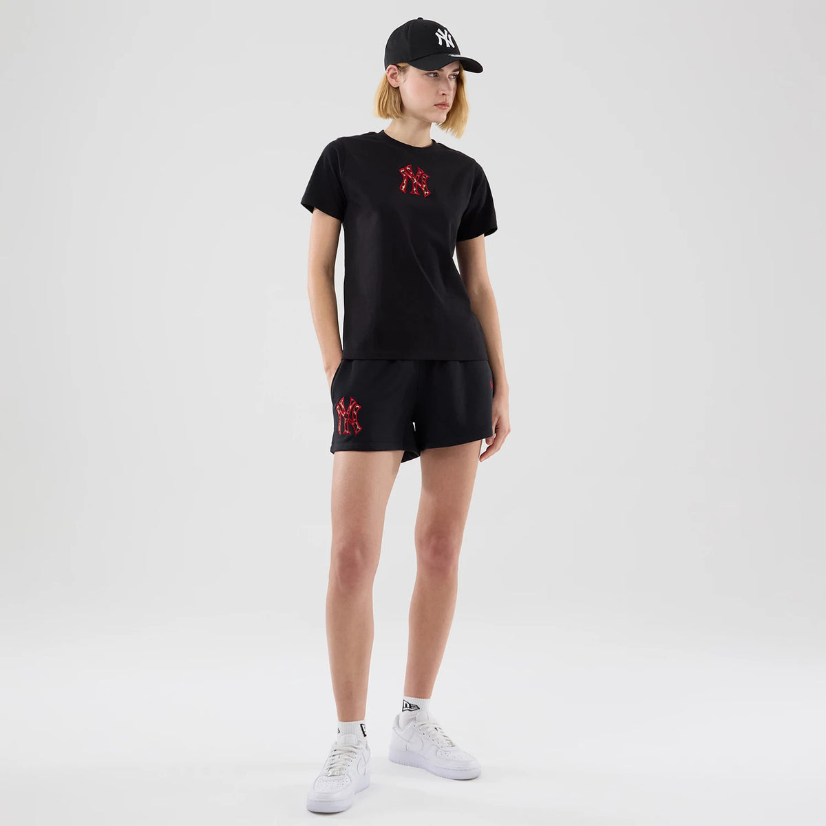 New Era New York Yankees Womens MLB Infill Black T-shirt, front view on a model paired with shorts, featuring a red and black infill Yankees logo prominently printed on the chest and sleeves fitting closely to the arms.