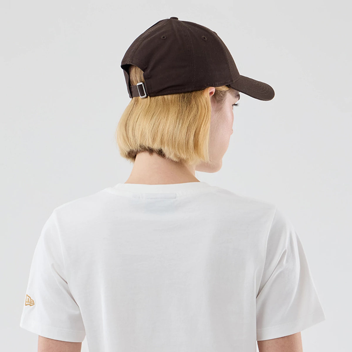 New Era New York Yankees Womens MLB Infill White T-shirt, back view showing a plain white surface with a gold embroidered New Era flag logo on the left sleeve, worn by a model styled with a dark cap.