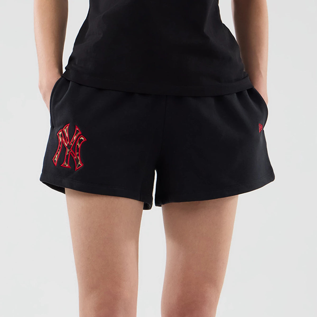 New Era New York Yankees Womens MLB Infill Black Shorts, front view on-model showing the black shorts with a red embroidered NY logo on the left thigh and a smaller embroidered New Era logo on the left pocket edge.