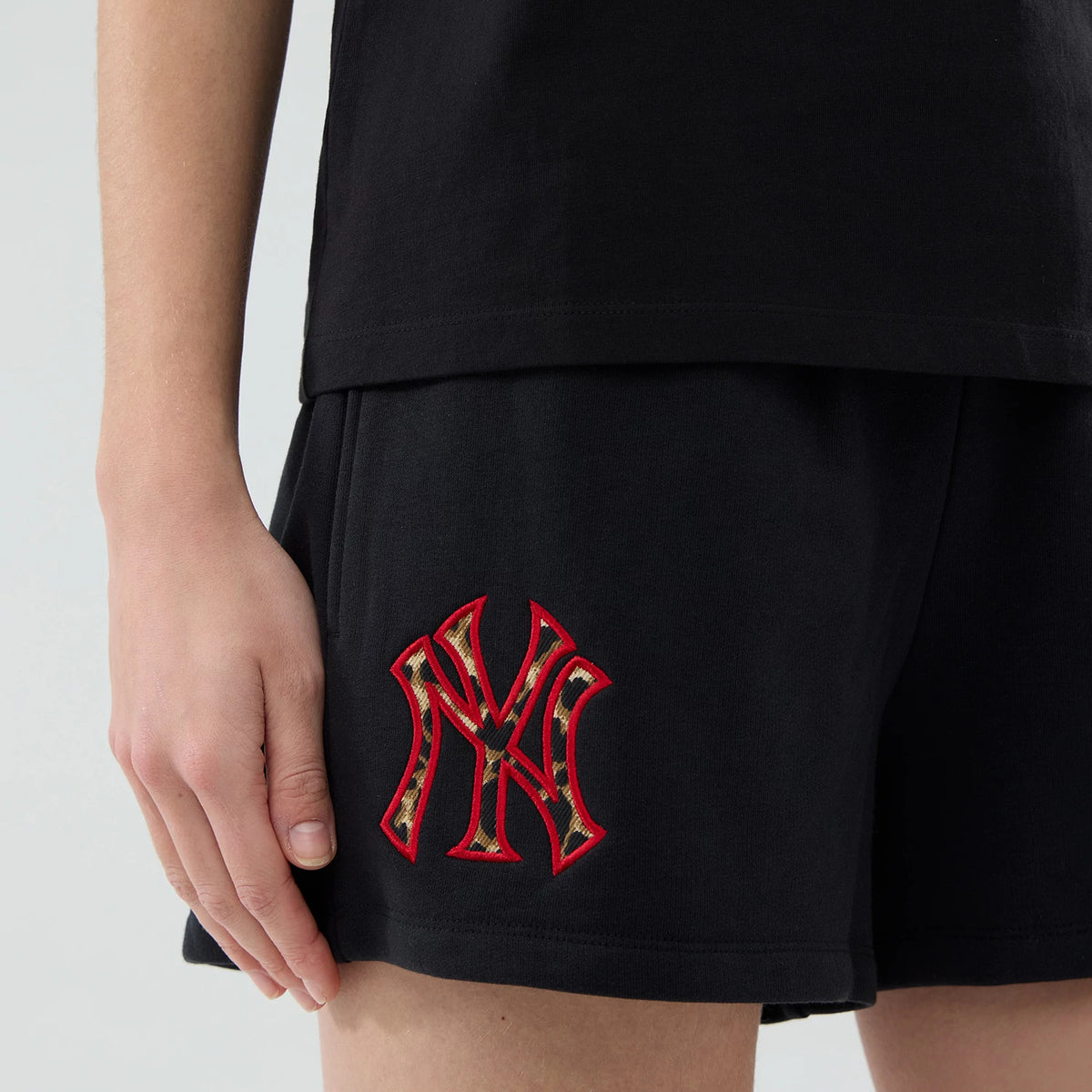 New Era New York Yankees Womens MLB Infill Black Shorts, three-quarter view showing the left leg with a large embroidered Yankees logo in red and camouflage pattern near the hem, worn with a matching black top.