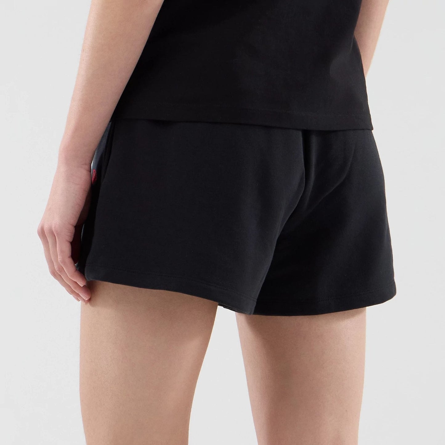 New Era New York Yankees Womens MLB Infill Black Shorts, back view on a model showing the plain black design with a hemline and a small embroidered Yankees logo on the side near the pocket.
