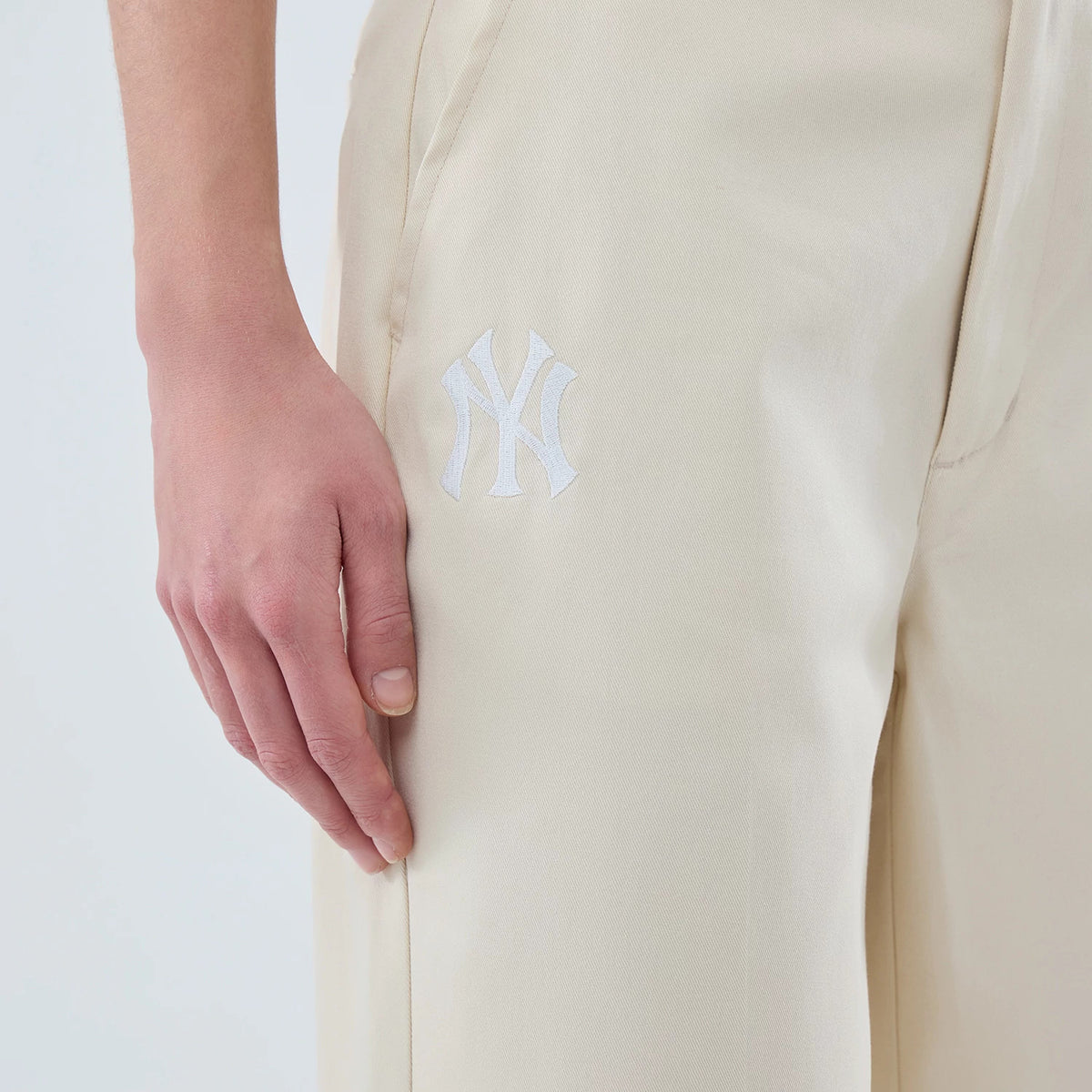 New Era New York Yankees Womens MLB Cream Chino Trousers, side view with a white embroidered NY logo on the upper right leg, showing cream fabric and the edge of a front pocket near the waistband.