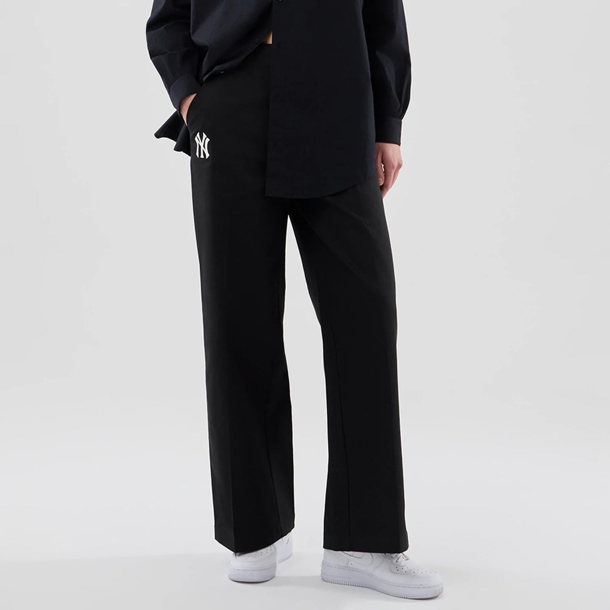 New Era New York Yankees Womens MLB Black Chino Trousers, front view on a model with a relaxed fit and wide legs, featuring the NY Yankees logo embroidered in white on the left pocket area, paired with white sneakers.