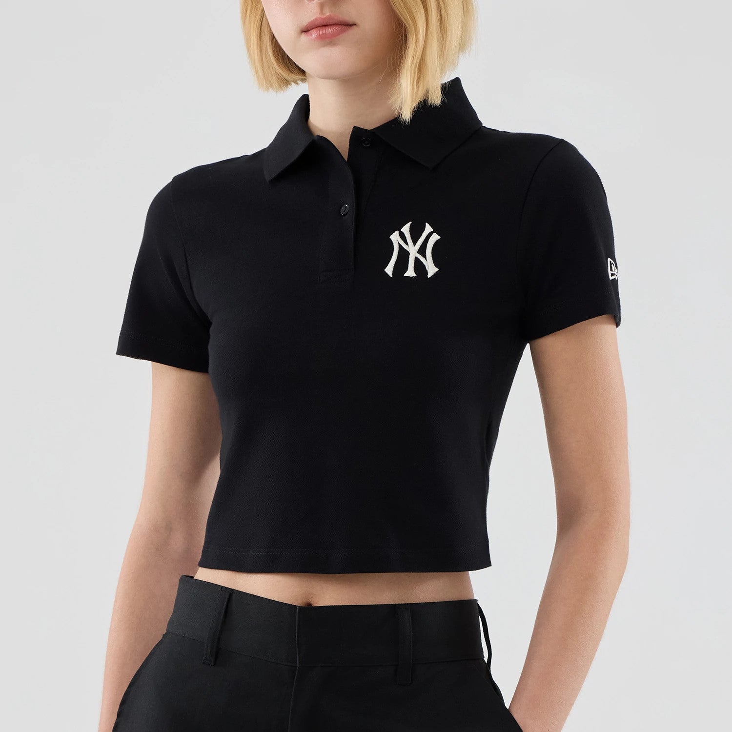 New Era New York Yankees Womens MLB Black Cropped Slim Polo T-shirt, front view on-model showing the white embroidered NY logo on the left chest and the New Era logo embroidered on the left sleeve against a black background.