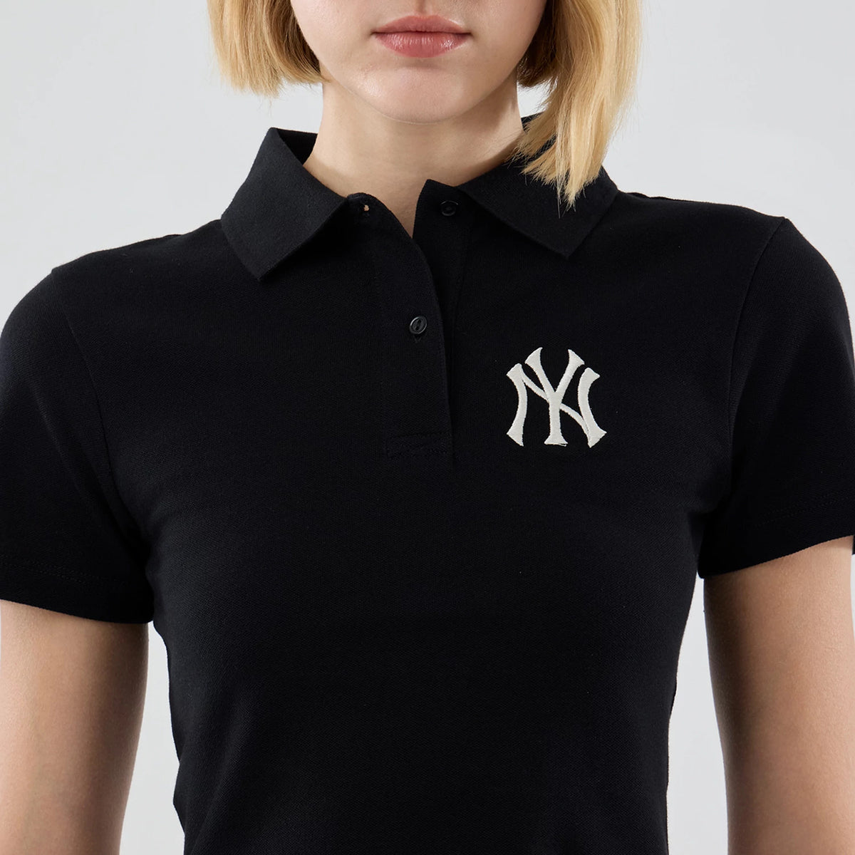 New Era New York Yankees Womens MLB Black Cropped Slim Polo T-shirt, front view showing a white embroidered NY logo on the left chest, a classic collar, and a button placket, styled with short sleeves on a model.
