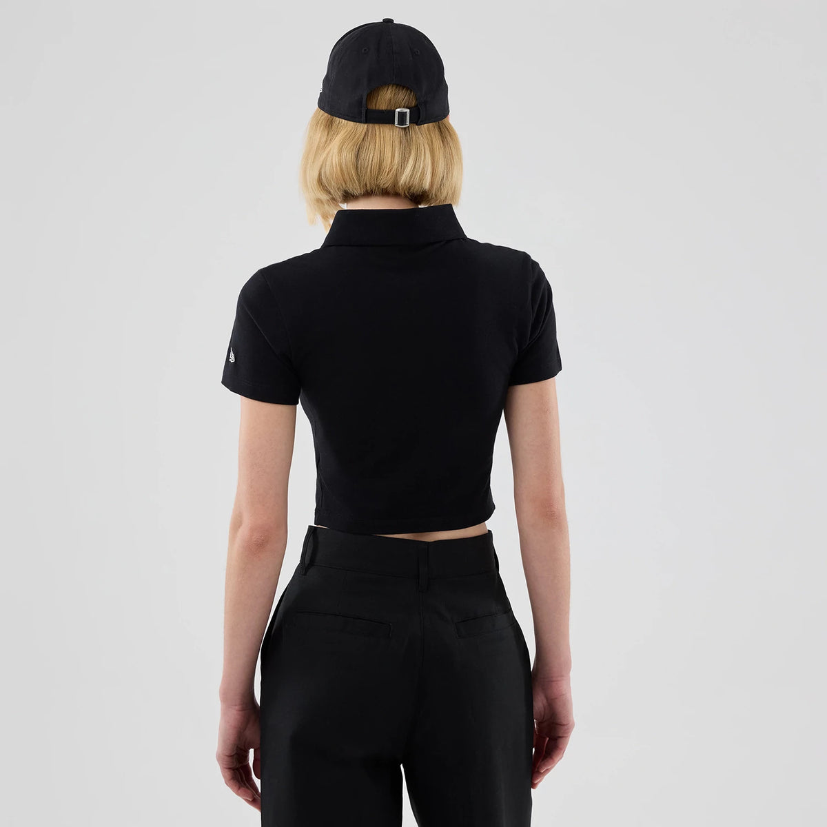 New Era New York Yankees Womens MLB Black Cropped Slim Polo T-shirt, back view on a model displaying the fitted black polo with short sleeves and a collar, an embroidered New Era logo on the left sleeve.