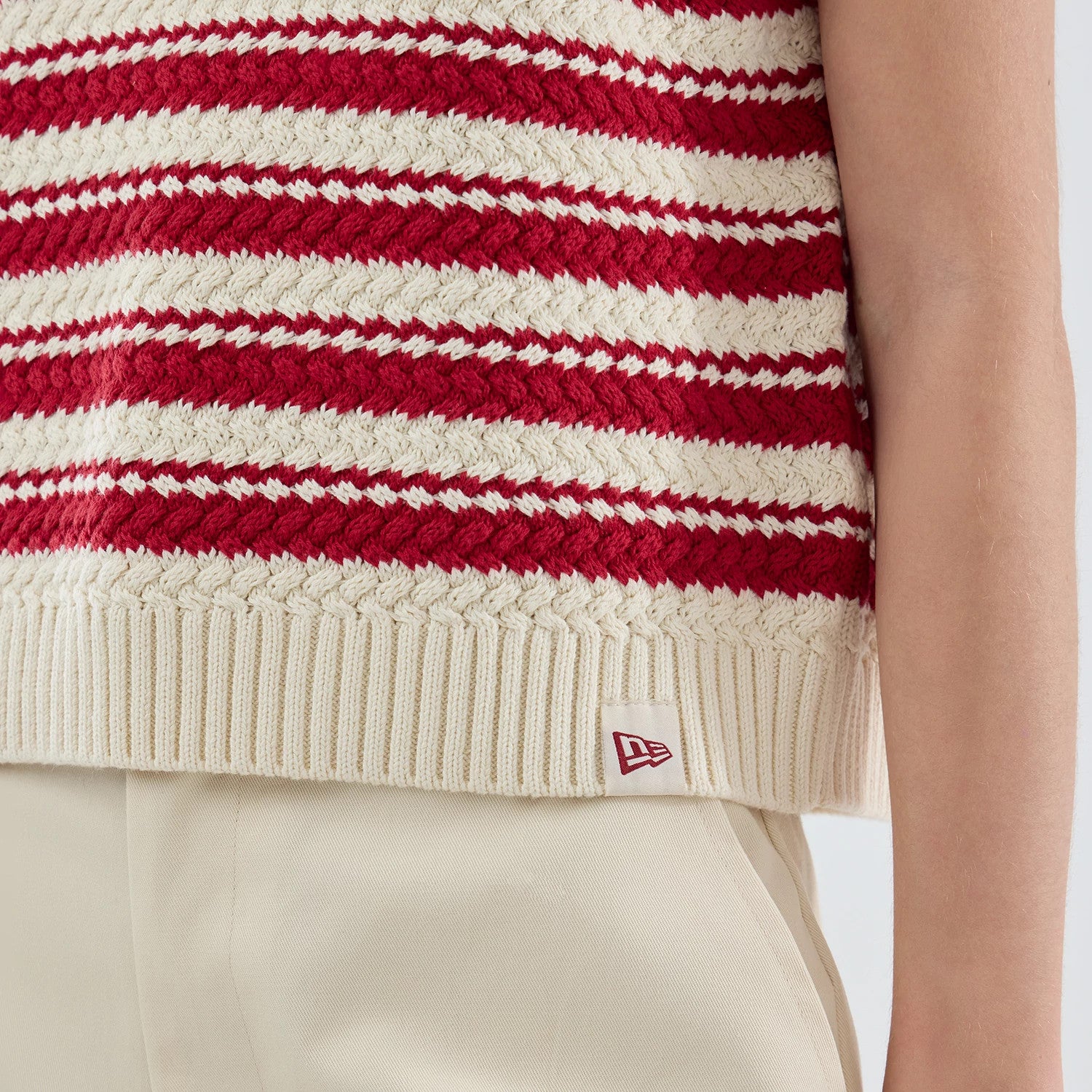 New Era New York Yankees Womens MLB Knit Stripe Dark Red Sleeveless V-neck Sweater, close-up showing red and cream horizontal knitted stripes with a ribbed hem, featuring the New Era flag logo tag near the side seam.