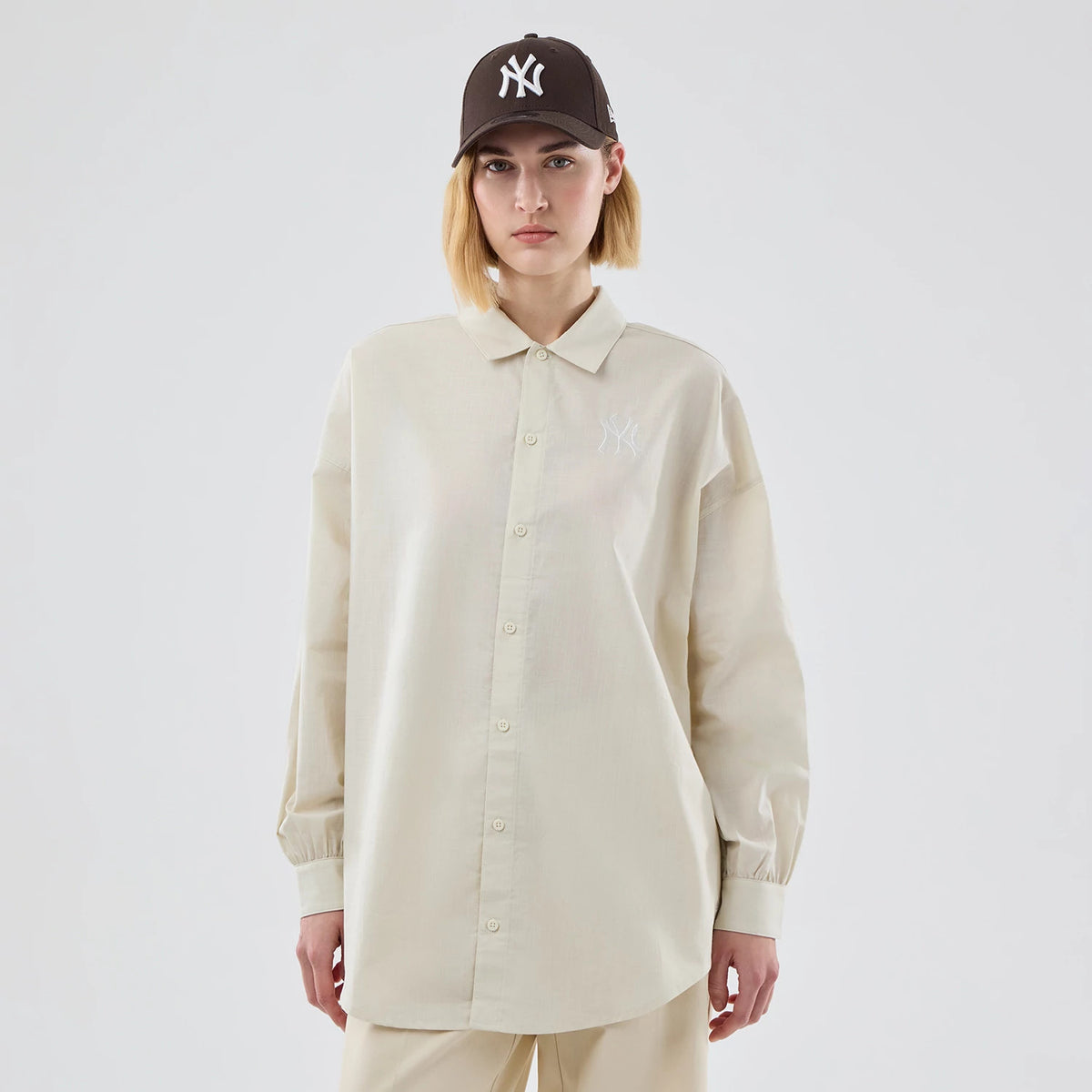 New Era New York Yankees Womens MLB Shirt Cream Long Sleeve Shirt, front view on a model wearing a matching cap, featuring a woven collar, button-down front, and the white embroidered NY logo on the left chest.