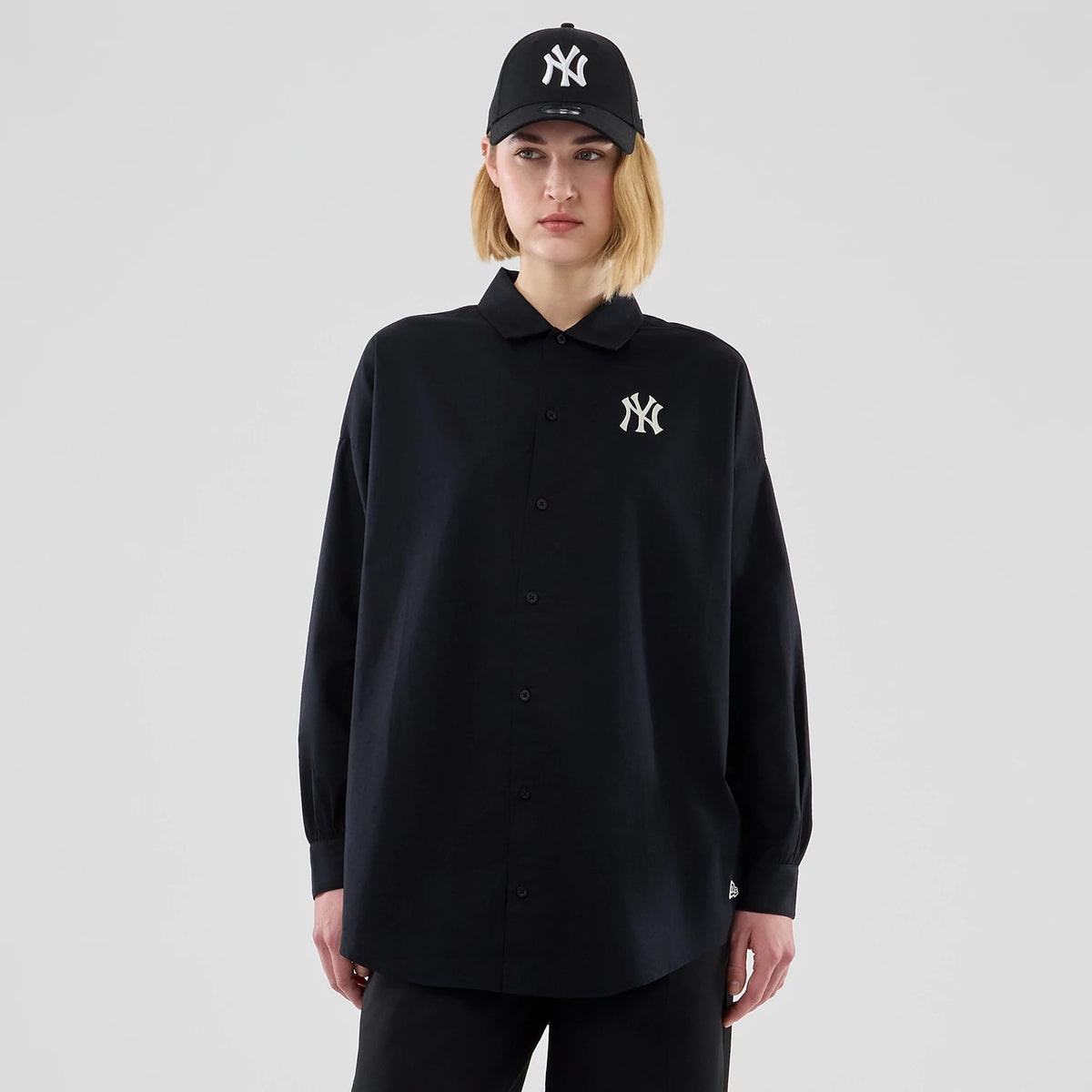 New Era New York Yankees Womens MLB Shirt Black Long Sleeve Shirt, front view on a model wearing a matching black cap, featuring an embroidered white NY logo on the left chest and a button-up design with a crisp collar.
