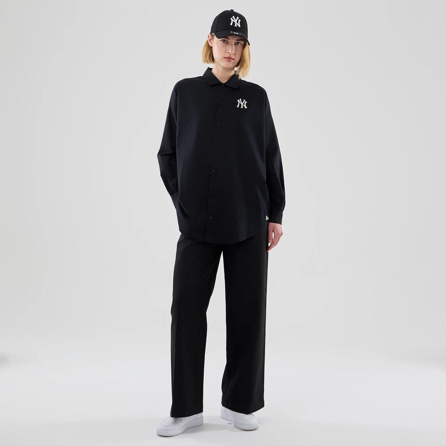 New Era New York Yankees Womens MLB Shirt Black Long Sleeve Shirt, front view on a model wearing a matching cap, featuring an embroidered white Yankees logo on the left chest and central button fastening on the long sleeve design.