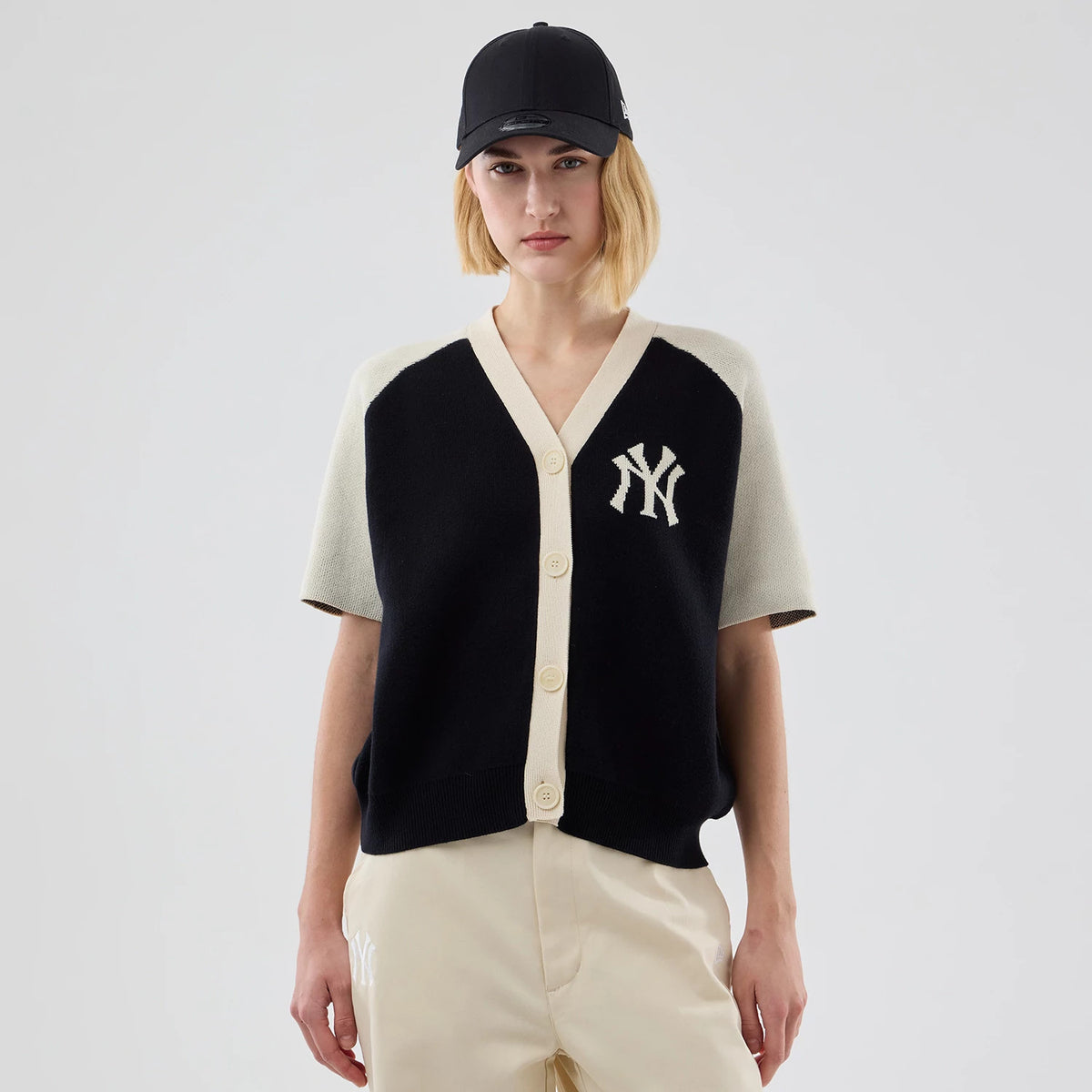 New Era New York Yankees Womens MLB Knit Stripe Black Short Sleeve Cardigan, front view on a model with a beige V-neck and button front, featuring an embroidered NY logo on the left chest, paired with beige trousers.