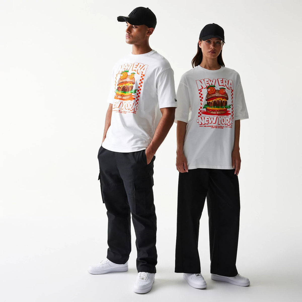 New Era Burger Food Graphic White Oversized T-Shirt, front view on-model, showcasing a large colourful burger graphic with New Era New York lettering, styled with black trousers and black caps.
