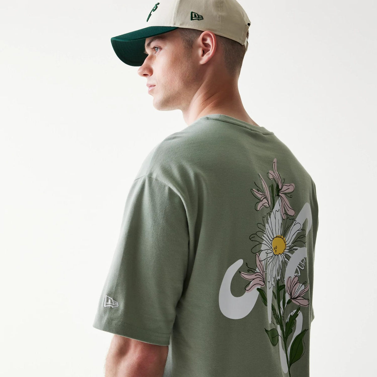 New Era Floral Graphic Pastel Green Oversized T-Shirt, back view on a model highlighting an intricate floral design featuring a large daisy with surrounding pink blooms, accompanied by a white graphic motif.