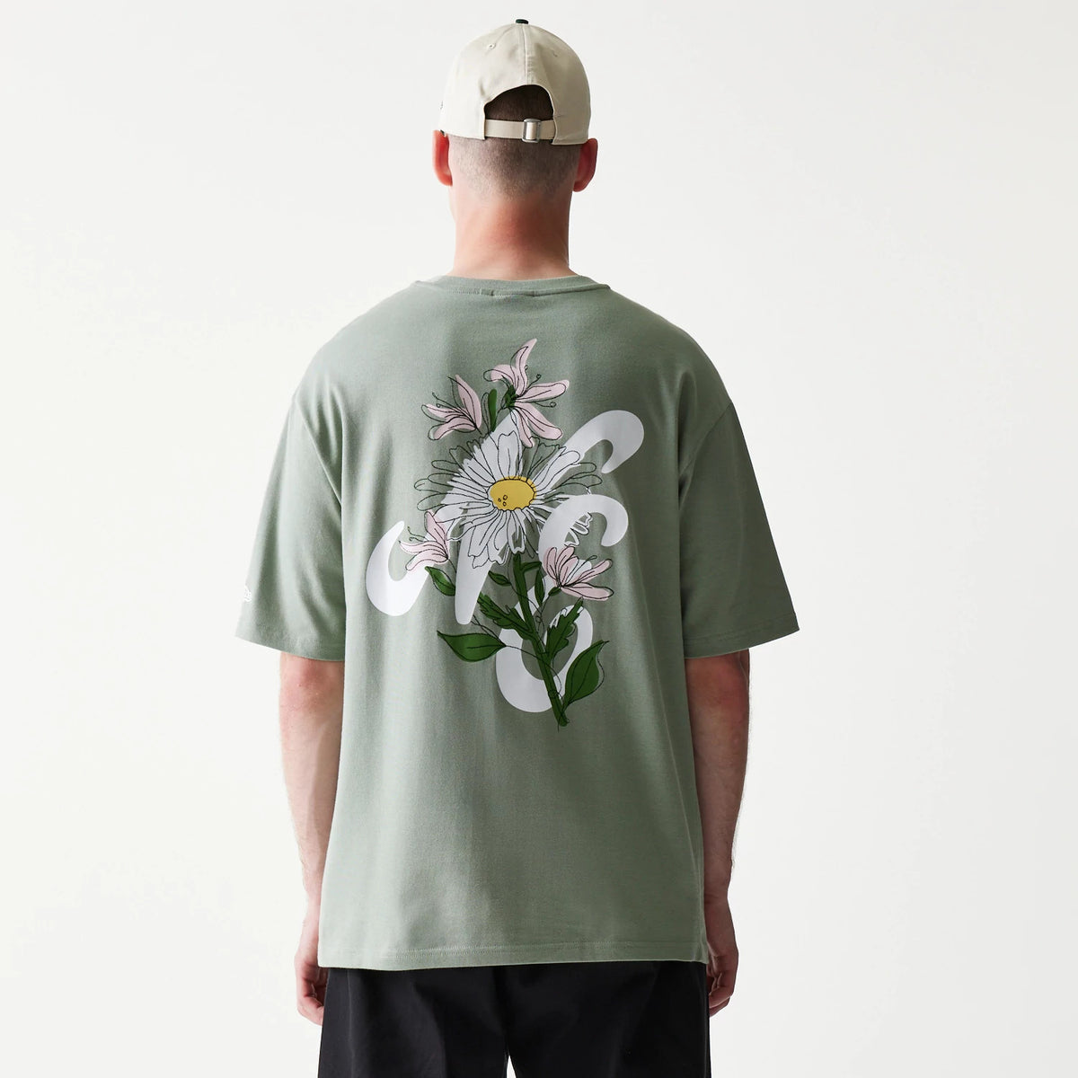 New Era Floral Graphic Pastel Green Oversized T-Shirt, back view on a model showing a large white and yellow floral graphic with green leaves and abstract shapes centred on the back of the pastel green fabric.