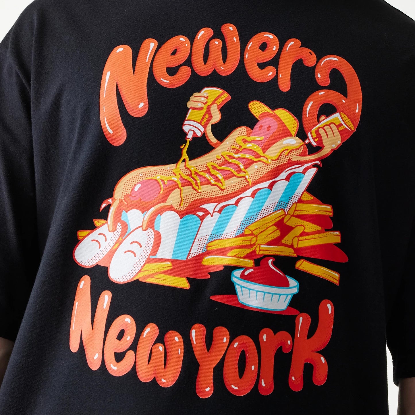 New Era Hotdog Food Graphic Black Oversized T-Shirt, back view showing a graphic of a hotdog with arms, surrounded by fries and sauce, above orange New Era New York lettering on the black fabric.