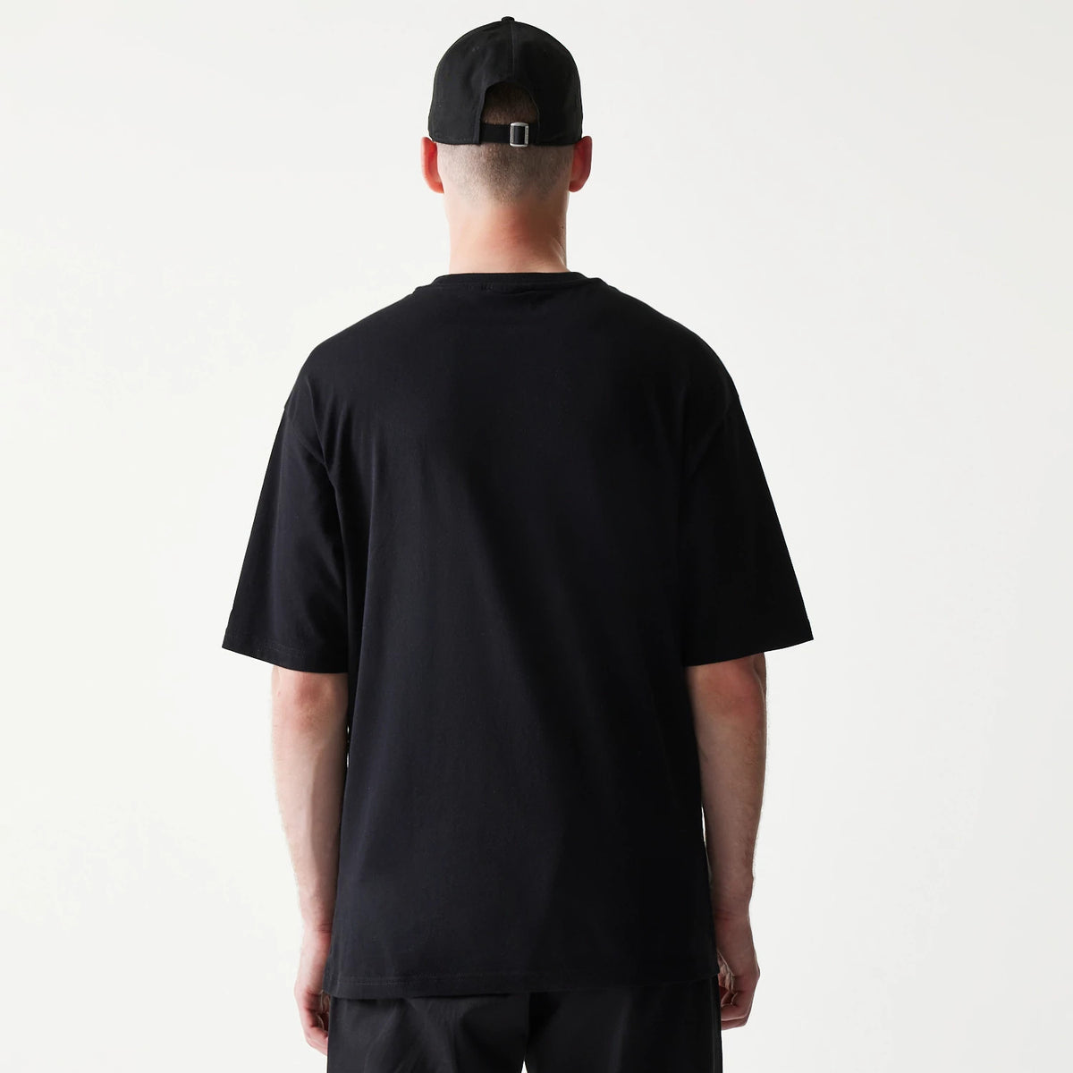 New Era Hotdog Food Graphic Black Oversized T-Shirt, back view on-model showing a plain black surface with an oversized fit, paired with a black cap that features an adjustable strap at the back.