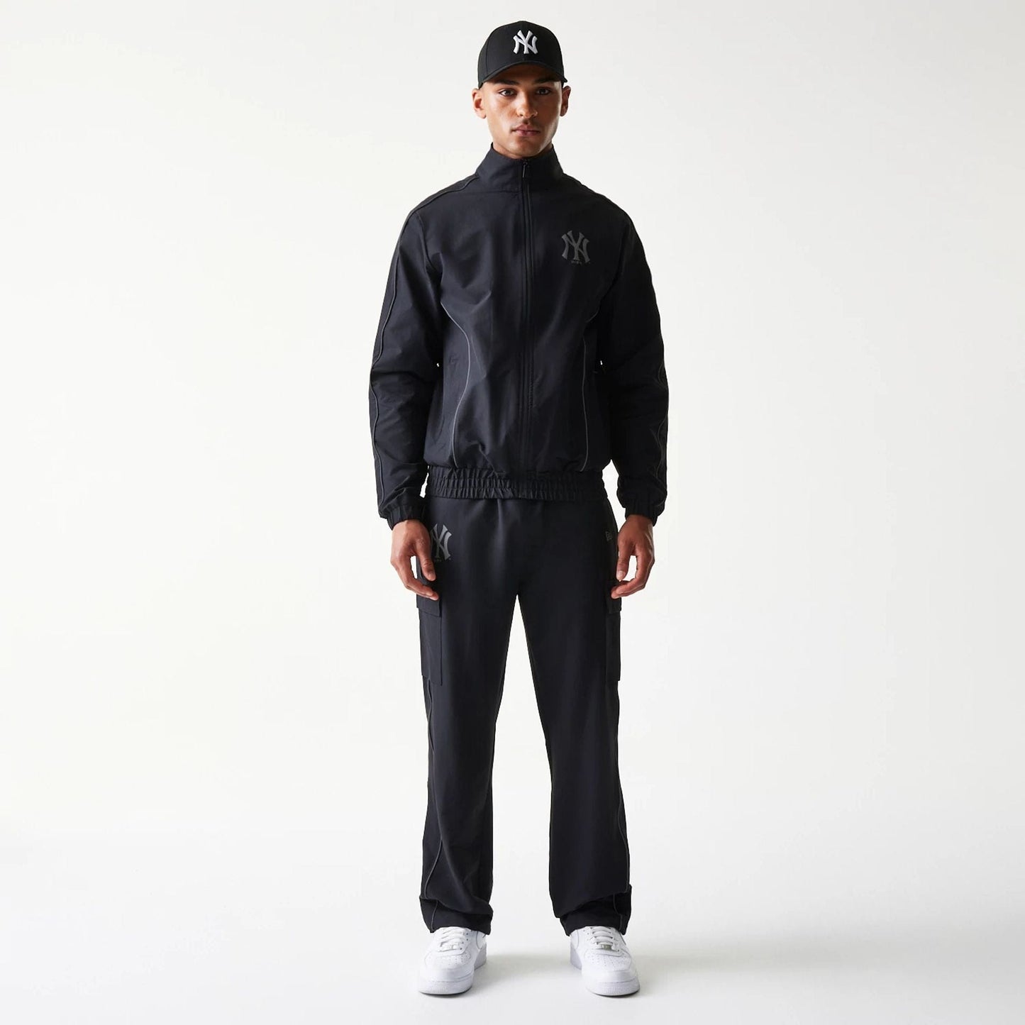New Era New York Yankees MLB Utility Black Straight Leg Cargo Joggers, front view on a model wearing a matching jacket and cap, showing black joggers with side cargo pockets and Yankees logo on the upper left thigh.