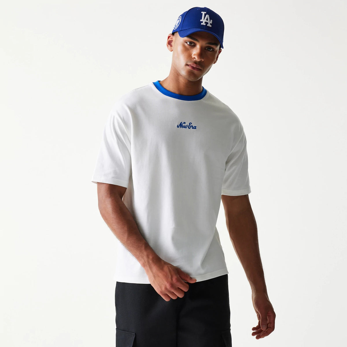 New Era Script White Oversized T-Shirt, front view on-model featuring a blue embroidered New Era logo on the chest, a blue neck trim and short sleeves complementing the relaxed white silhouette.