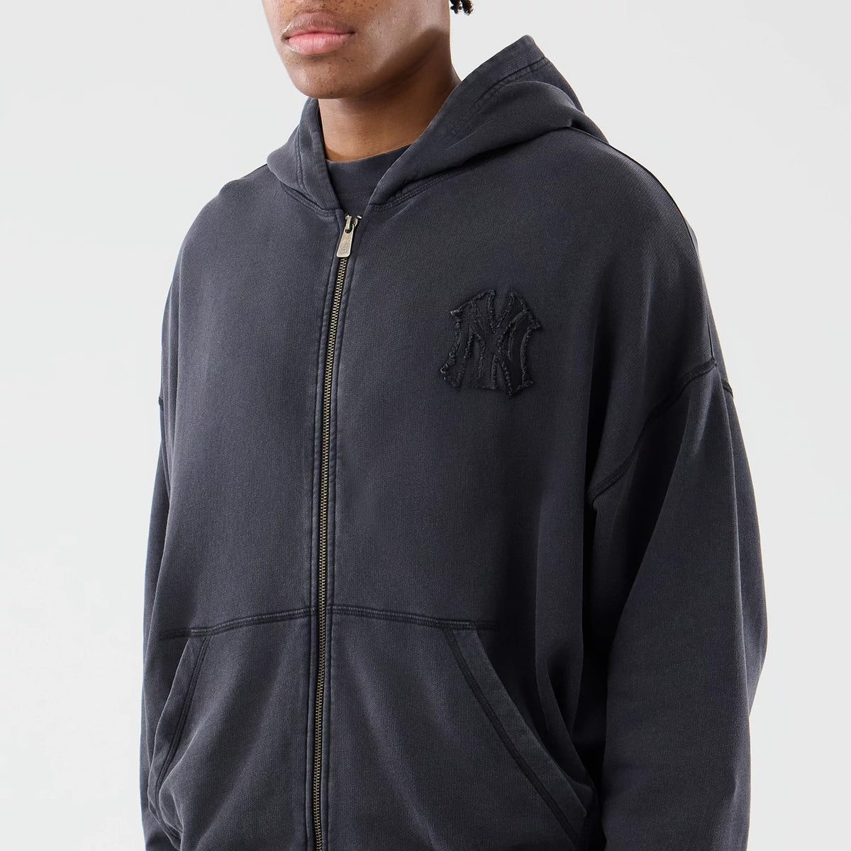 New Era New York Yankees MLB Washed Black Full Zip Hoodie, front three-quarter view showing the dark zip up the centre, a raised Yankees logo embroidered on the left chest, and worn on a model with the hood down.