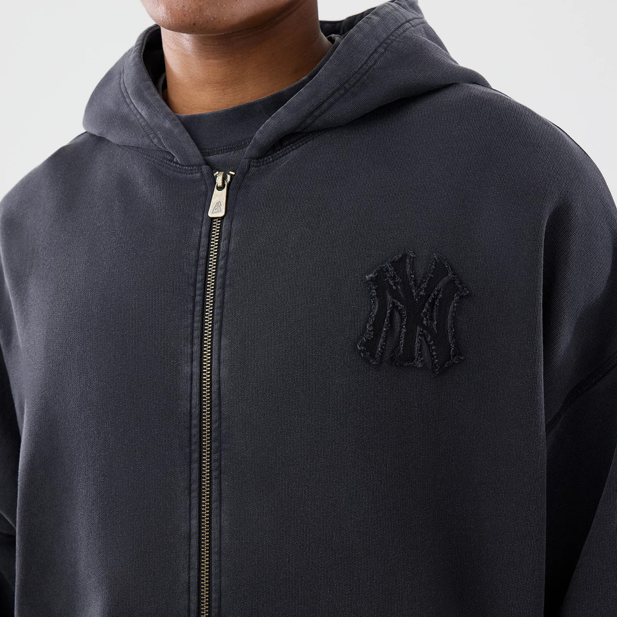New Era New York Yankees MLB Washed Black Full Zip Hoodie, front view on a model displaying the black embroidered NY logo on the left chest and a full-length zip closure in the centre of the washed black fabric.