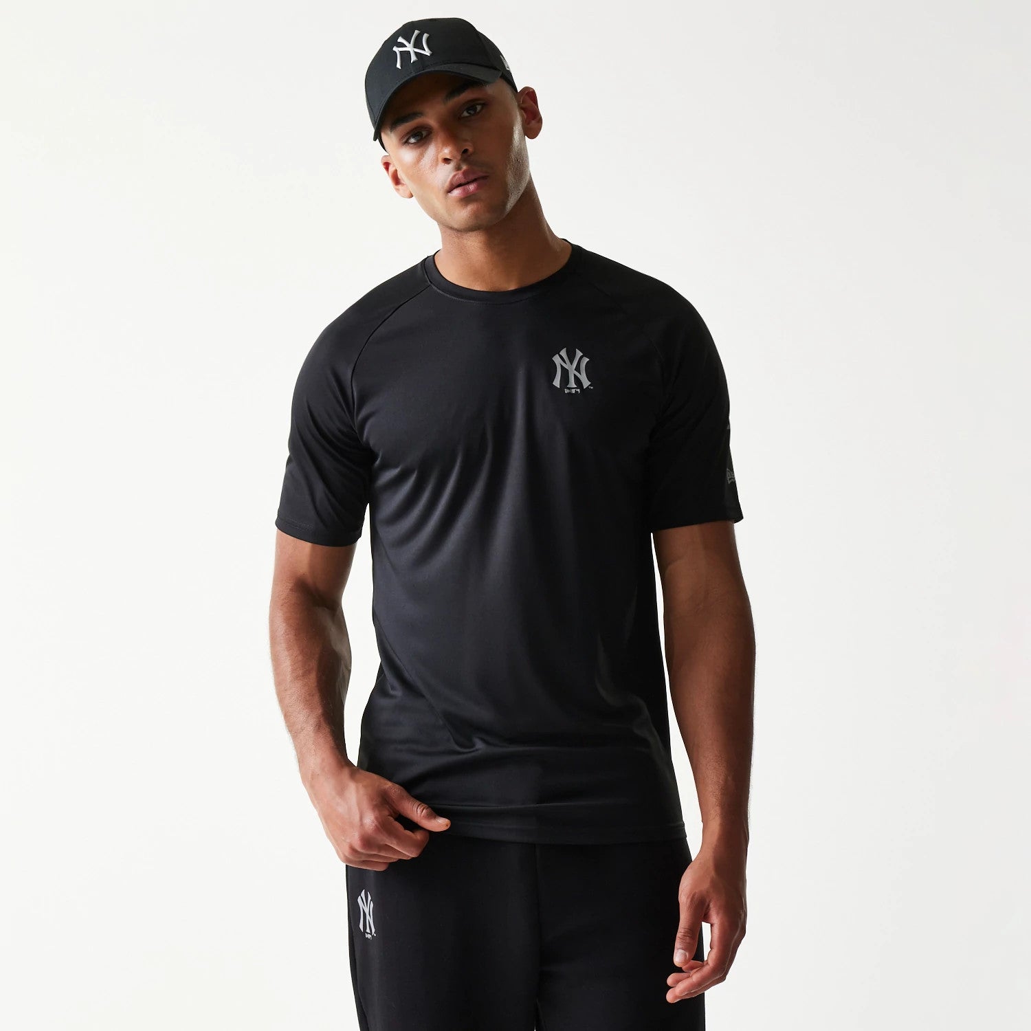 New Era New York Yankees MLB Reflective Black T-Shirt, front view on-model featuring a reflective embroidered New York Yankees logo on the left chest, styled with matching black shorts also displaying the logo on the left leg.