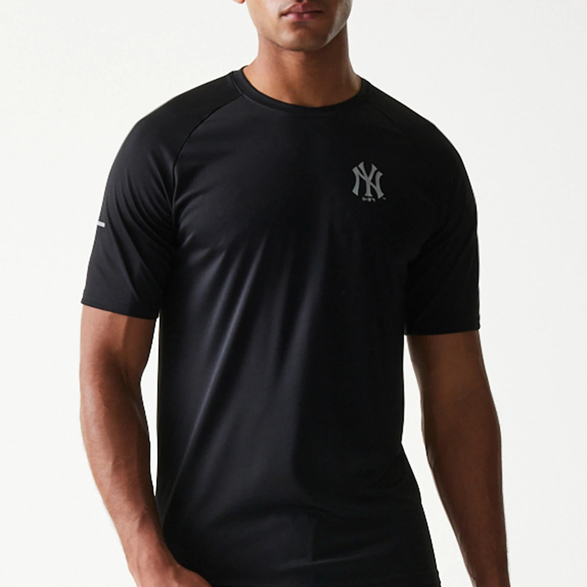 New Era New York Yankees MLB Reflective Black T-Shirt, front view on a model showing a reflective printed New York Yankees logo on the left chest, with short sleeves and a rounded neck design.