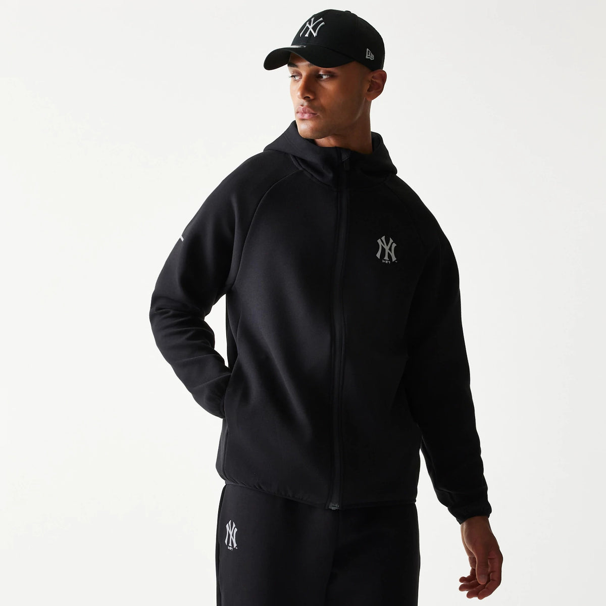New Era New York Yankees MLB Black Full Zip Hoodie, front view on-model showing the black hoodie with a full zip and the raised New York Yankees logo on the left chest, paired with matching black trousers featuring the same logo.