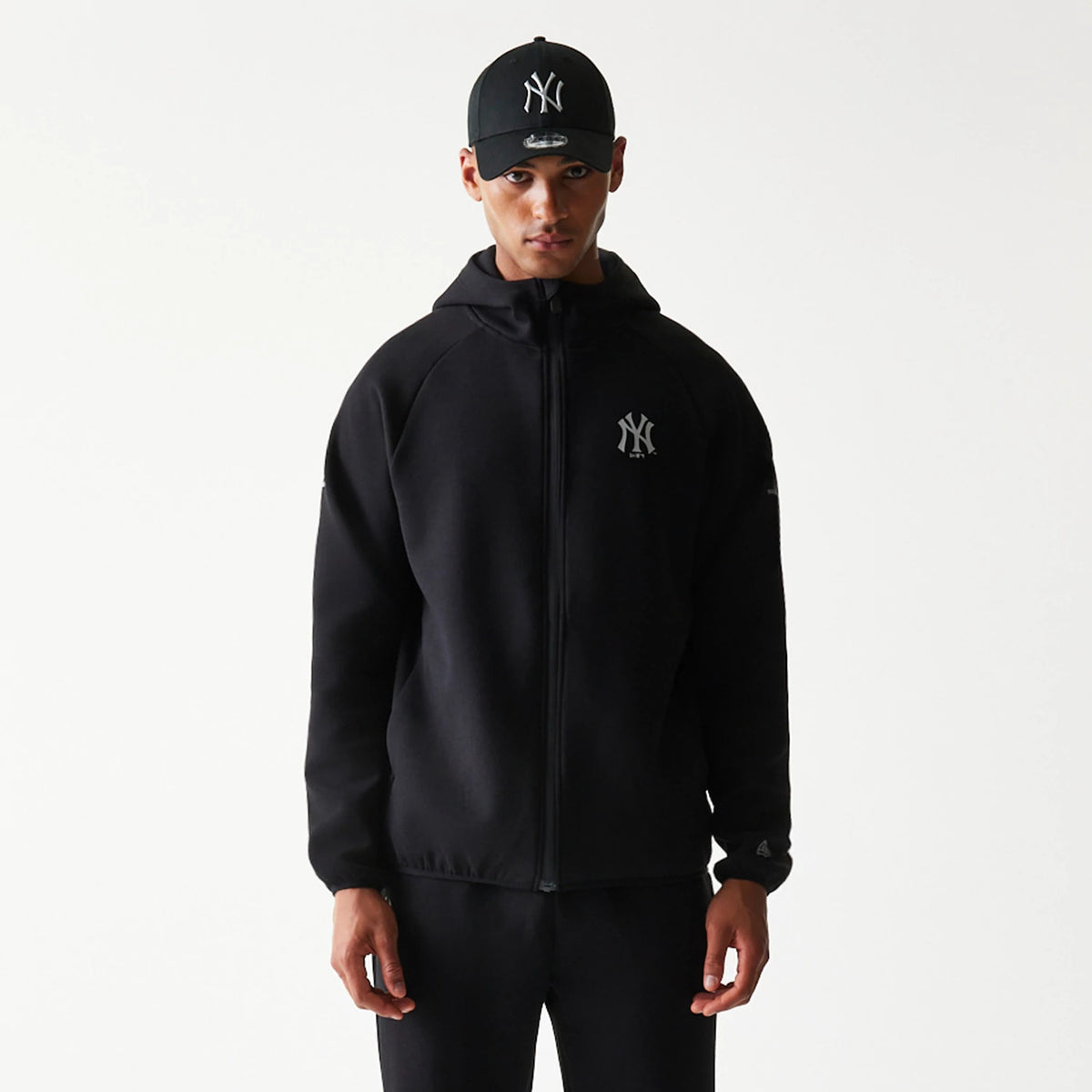 New Era New York Yankees MLB Black Full Zip Hoodie, front view on-model showcasing the black hoodie with a full zip closure, featuring an embroidered New York Yankees logo on the left chest and a hood covering the back of the neck.