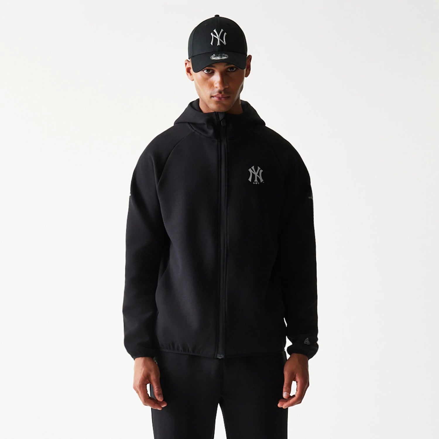 New Era New York Yankees MLB Black Full Zip Hoodie, front view on-model showcasing the black hoodie with a full zip closure, featuring an embroidered New York Yankees logo on the left chest and a hood covering the back of the neck.