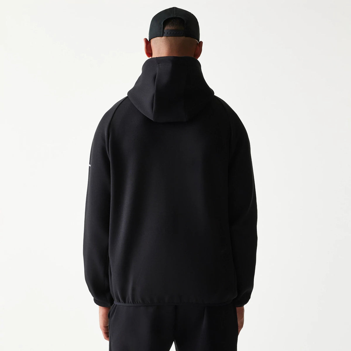 New Era New York Yankees MLB Black Full Zip Hoodie, back view on a model with a matching black cap, showing the plain black hood and relaxed fit of the hoodie, with a small embroidered logo positioned on the upper left sleeve.