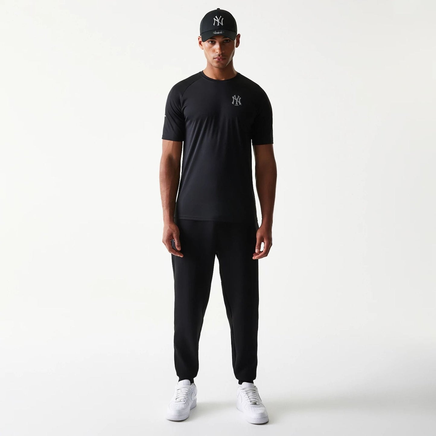 New Era New York Yankees MLB Black Joggers, front view on a model with a matching black New York Yankees cap and T-shirt, showing elasticated cuffs and a relaxed fit, paired with white trainers.