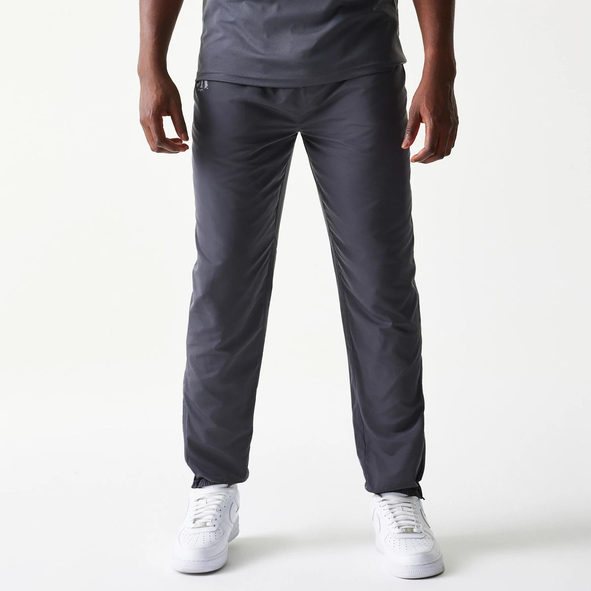 New Era New York Yankees MLB Dark Grey Track Pants, front view on a model wearing white trainers and a matching dark grey top, showing the relaxed fit and elasticated waistband with Yankees logo detail near the hip.