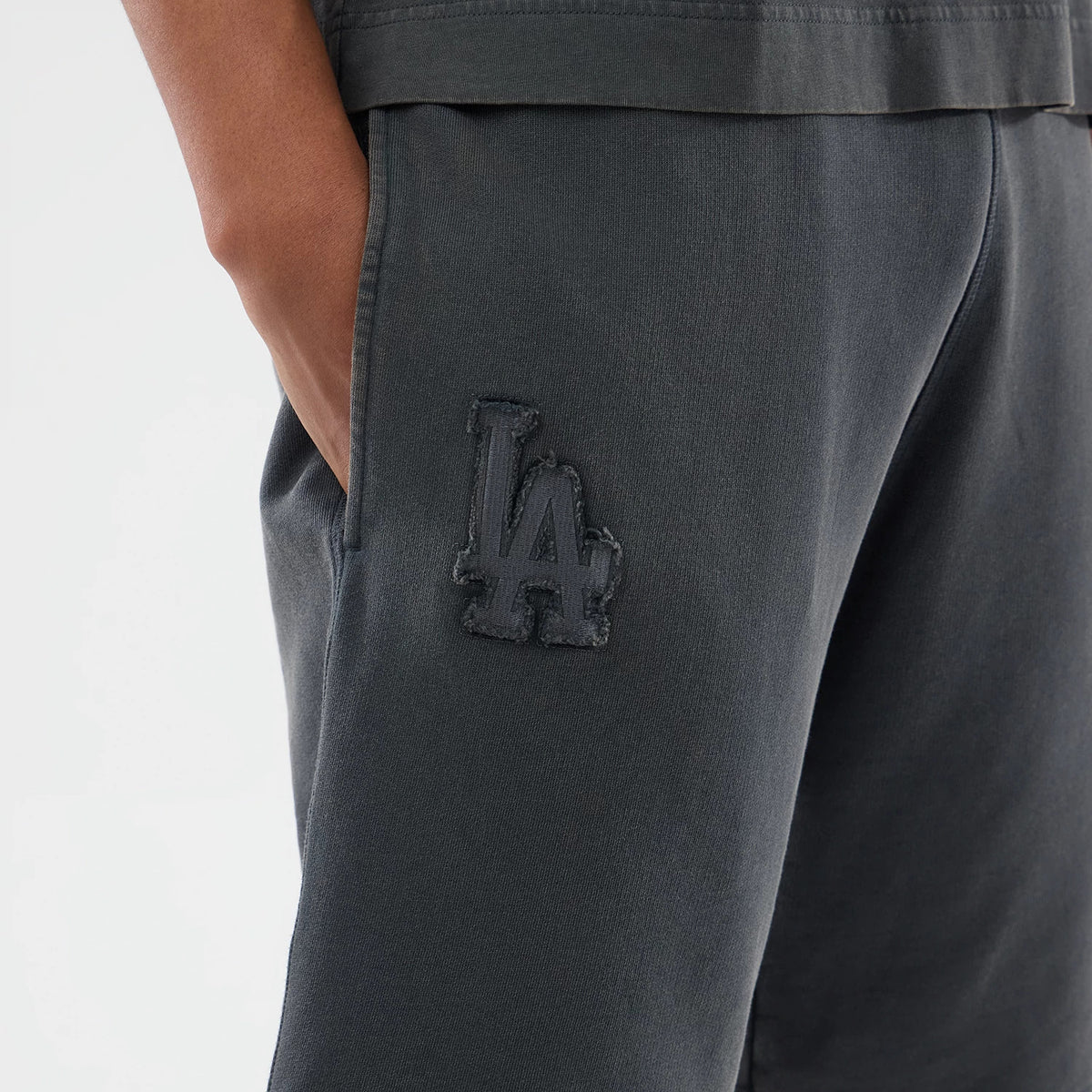 New Era LA Dodgers MLB Washed Dark Grey Shorts, three-quarter view showing a dark grey textured LA logo embroidered on the left leg near the pocket, with a relaxed fit seen on the model's upper leg.