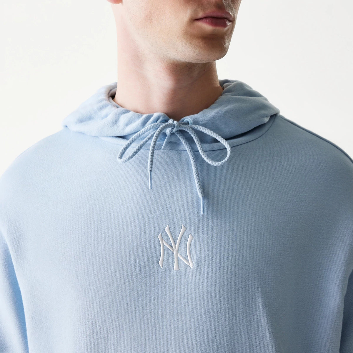 New Era New York Yankees MLB Midi Pastel Blue Oversized Pullover Hoodie, front view on-model showing the light blue hood with drawstrings and a white embroidered Yankees logo centred on the chest.